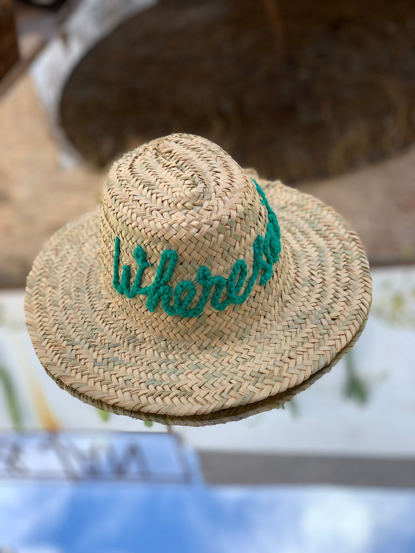 A straw hat embroidered Wheresnik, resting at the edge of a pool