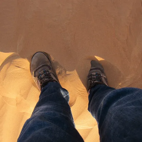 Suede walking shoes sinking into red desert sand