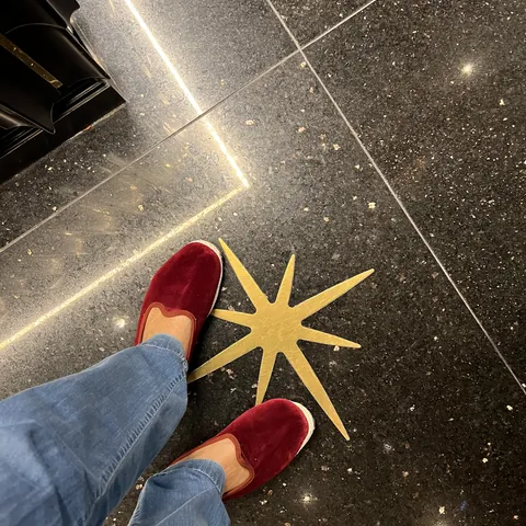 Red loafers on black granite with an inlaid brass star