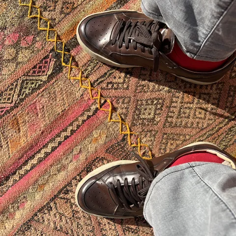 Dark leather sneakers on a red kilim laid over the sand at Habitas AlUla