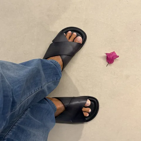 Black leather sandals on pale stone with a fallen bougainvillea flower