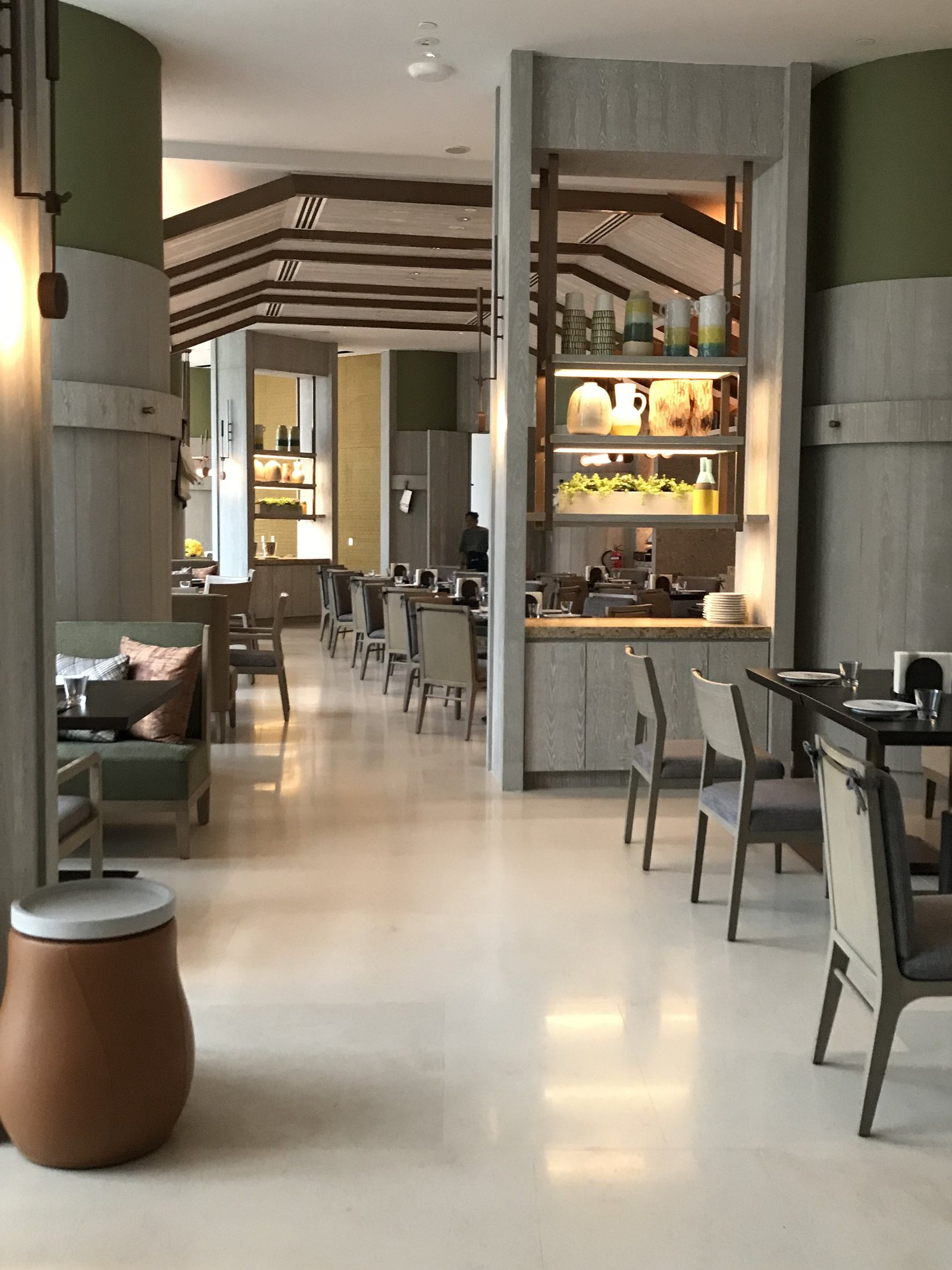 A dining room in pale stone and green timber with tables set along a window wall