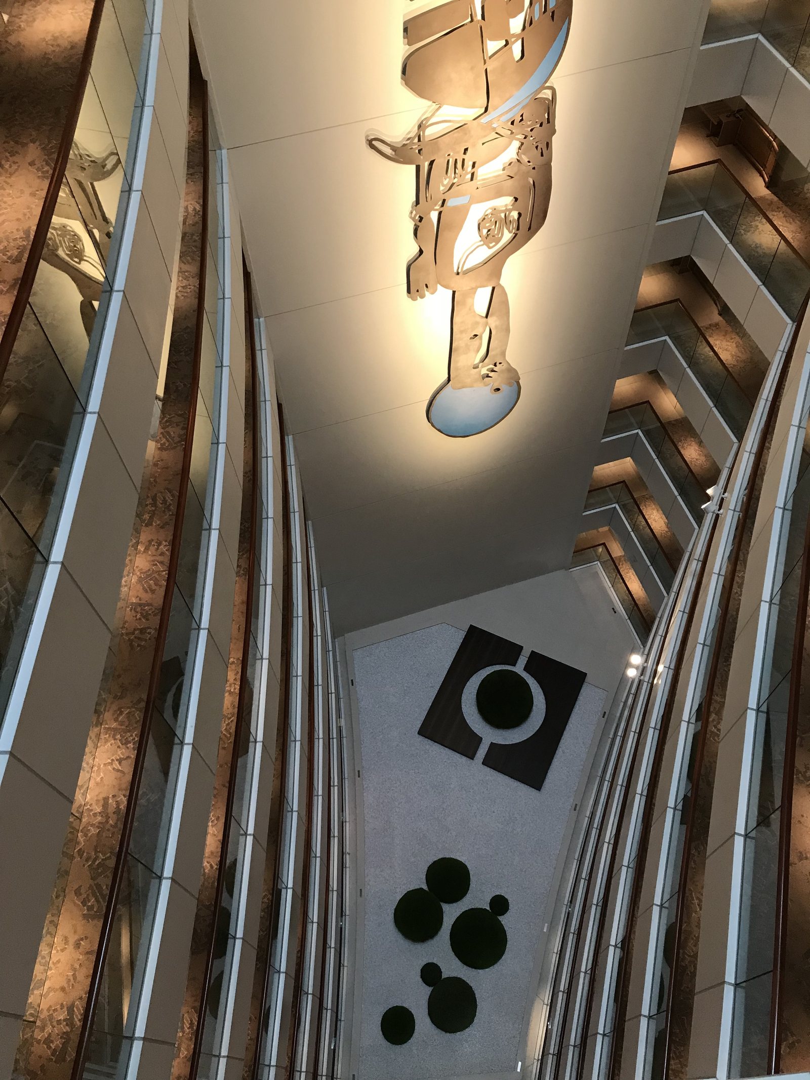 An atrium with stepped balconies lit in bands, seen looking down