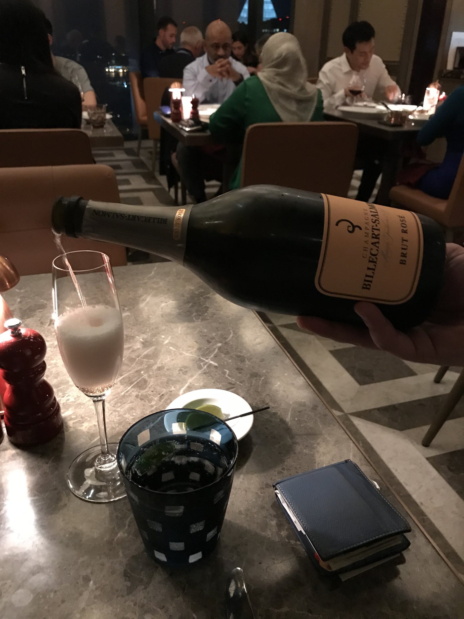 A bottle of Billecart-Salmon on a marble table with a flute and a cocktail beside it