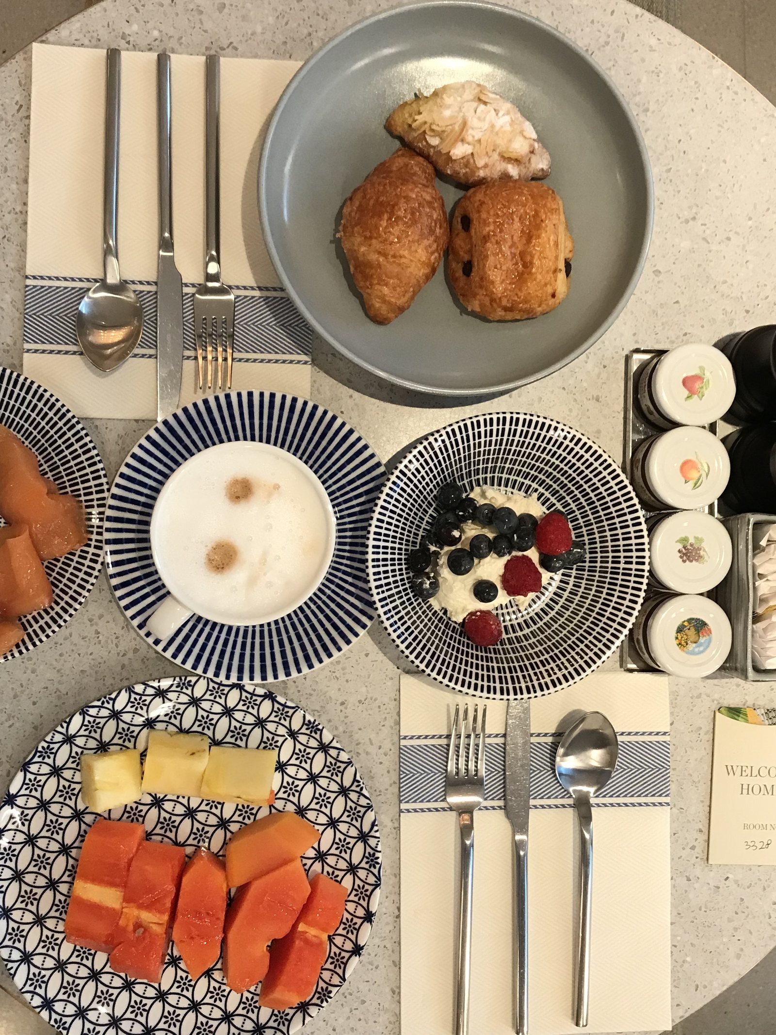 A breakfast table from above with pastries, papaya, yoghurt and coffee on patterned plates
