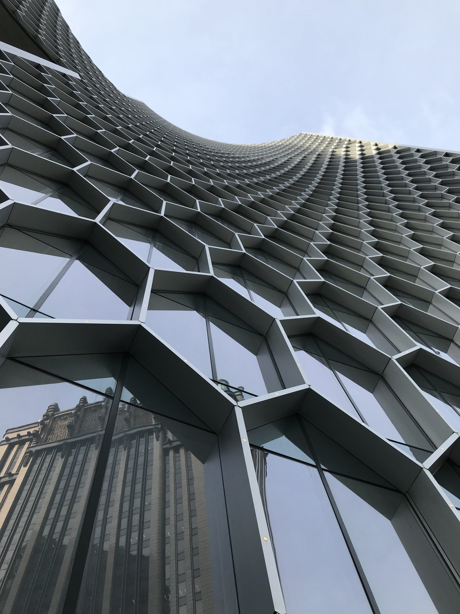 The honeycomb facade of the DUO Towers seen from the street below, the panels folding against the sky
