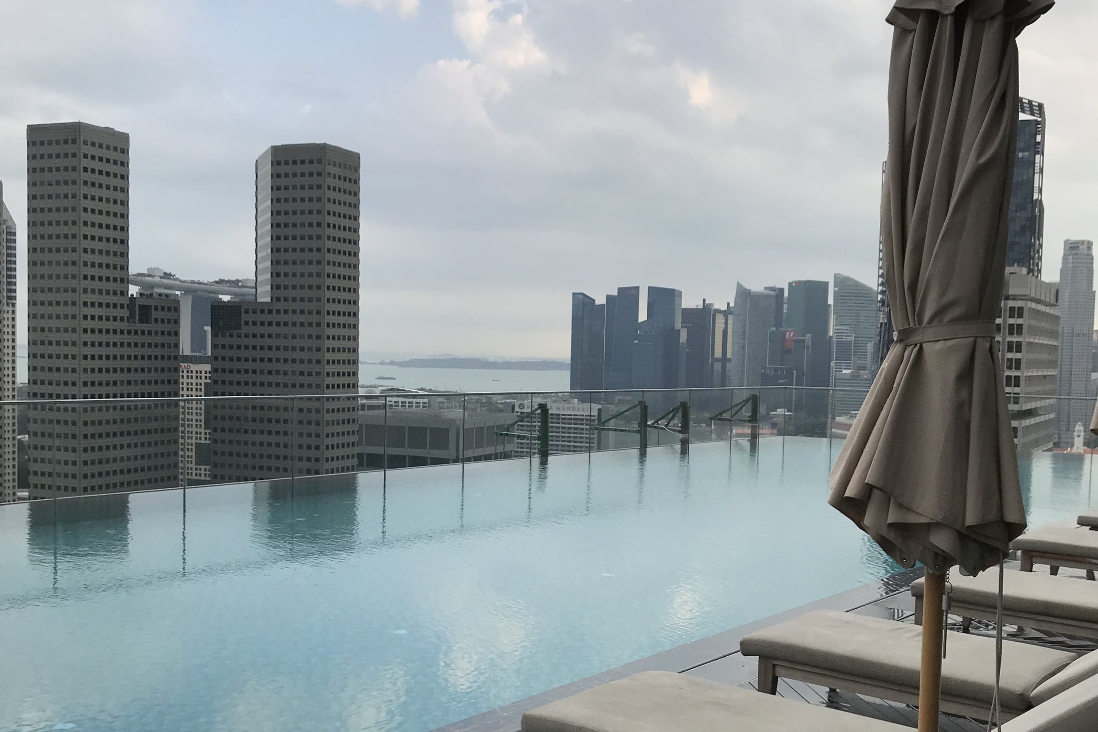 A twenty-five metre infinity pool on a high terrace, loungers along one side and the towers of Singapore behind it