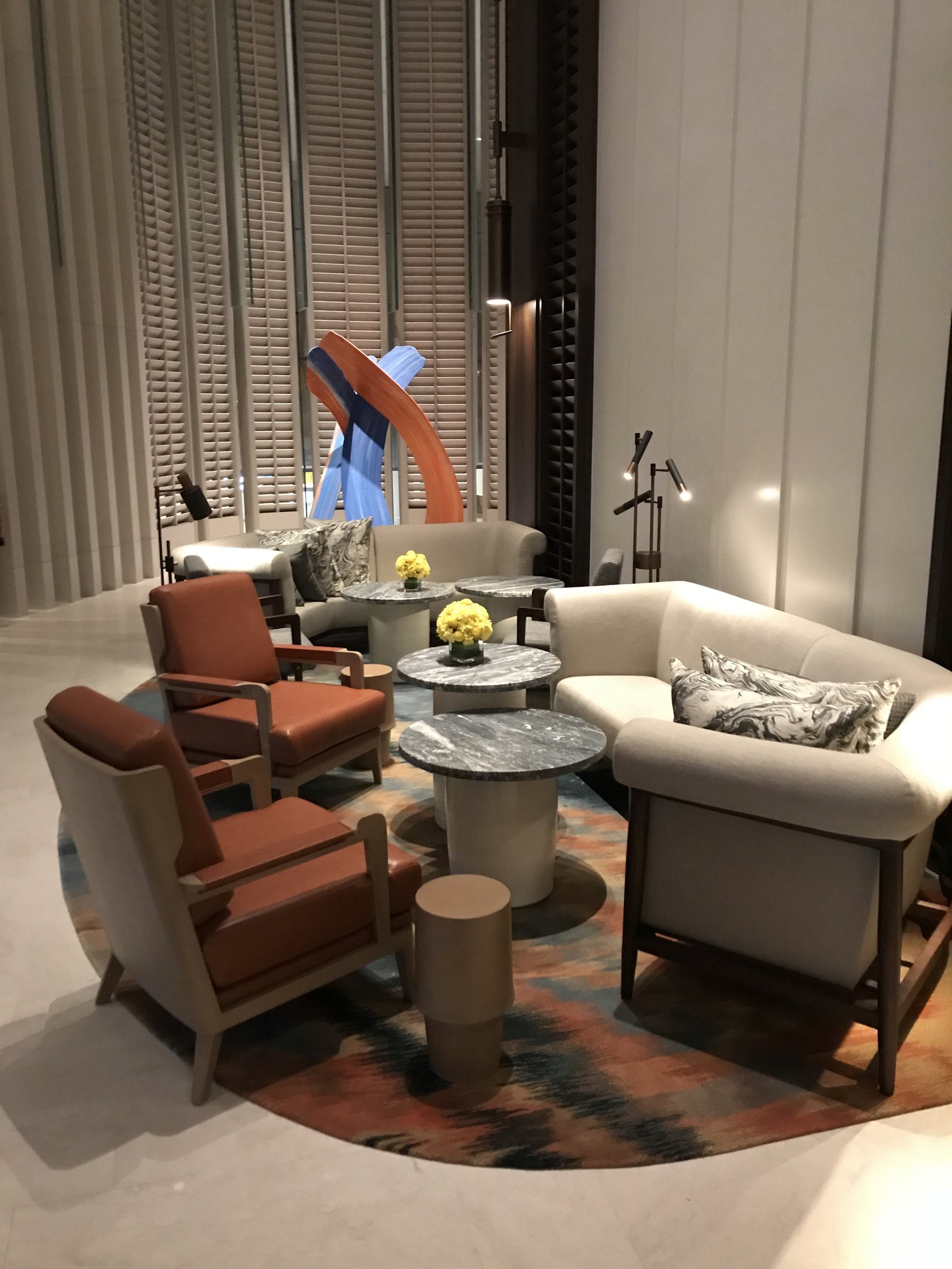 A lounge with cream armchairs and a patterned rug, a sculpture on a low table