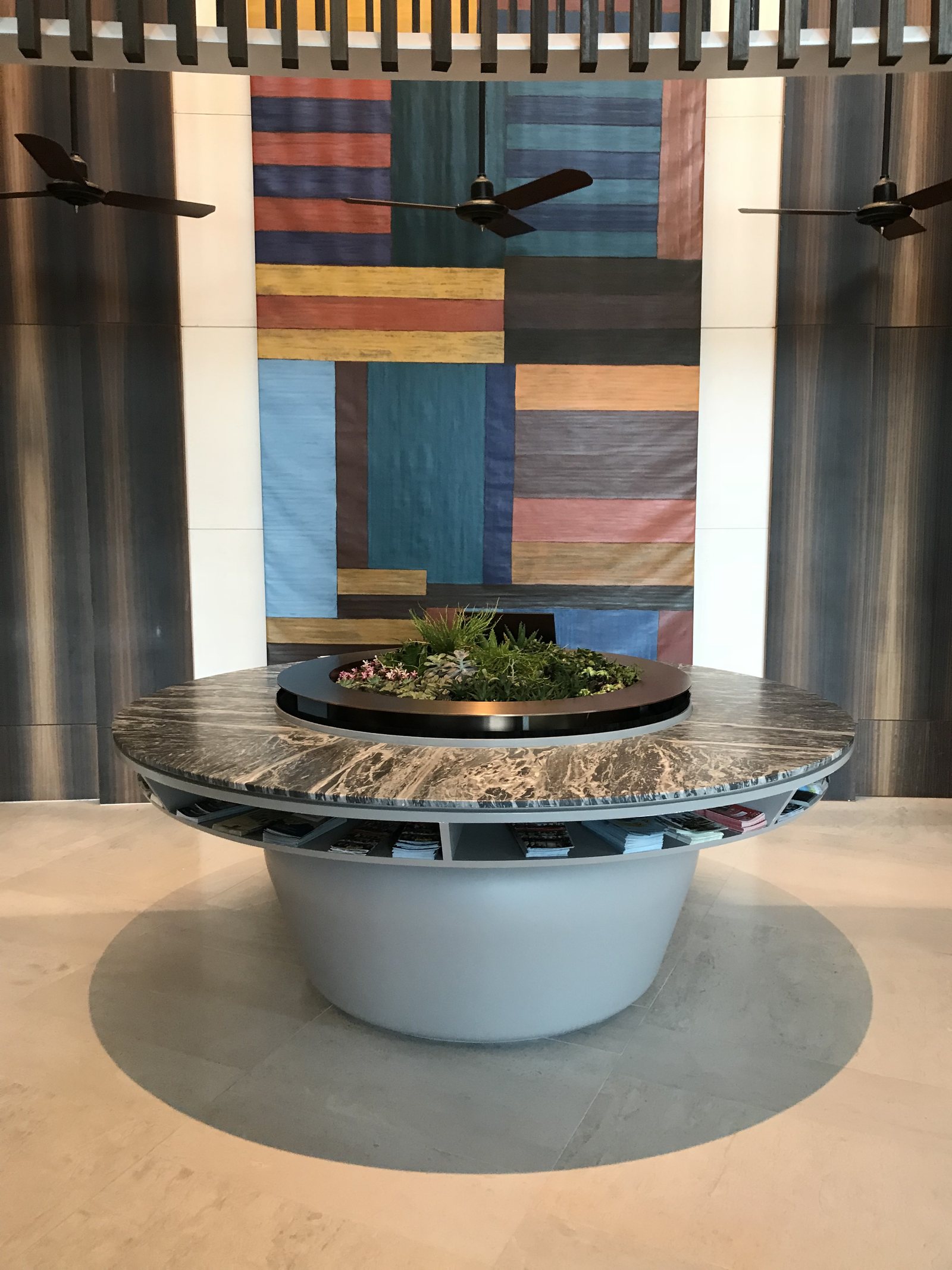 A round planted installation on a stone base in front of a tall woven hanging