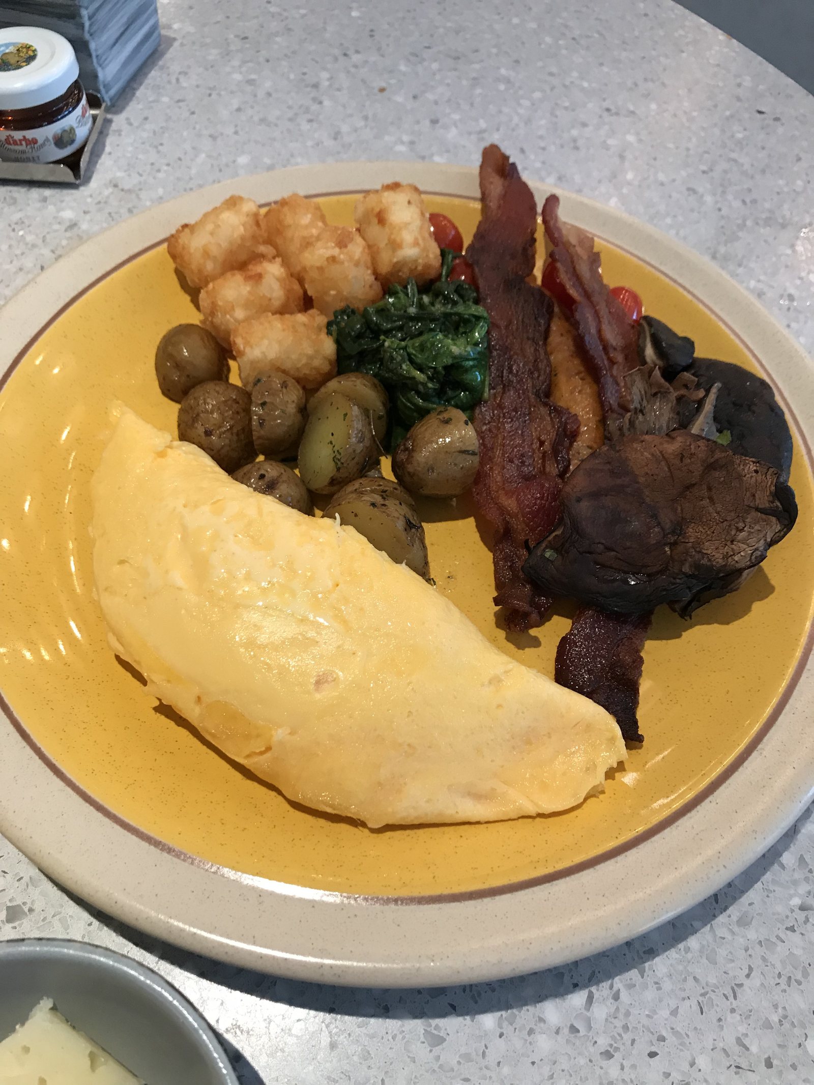 An omelette with bacon, olives, spinach and potatoes on a yellow-rimmed plate