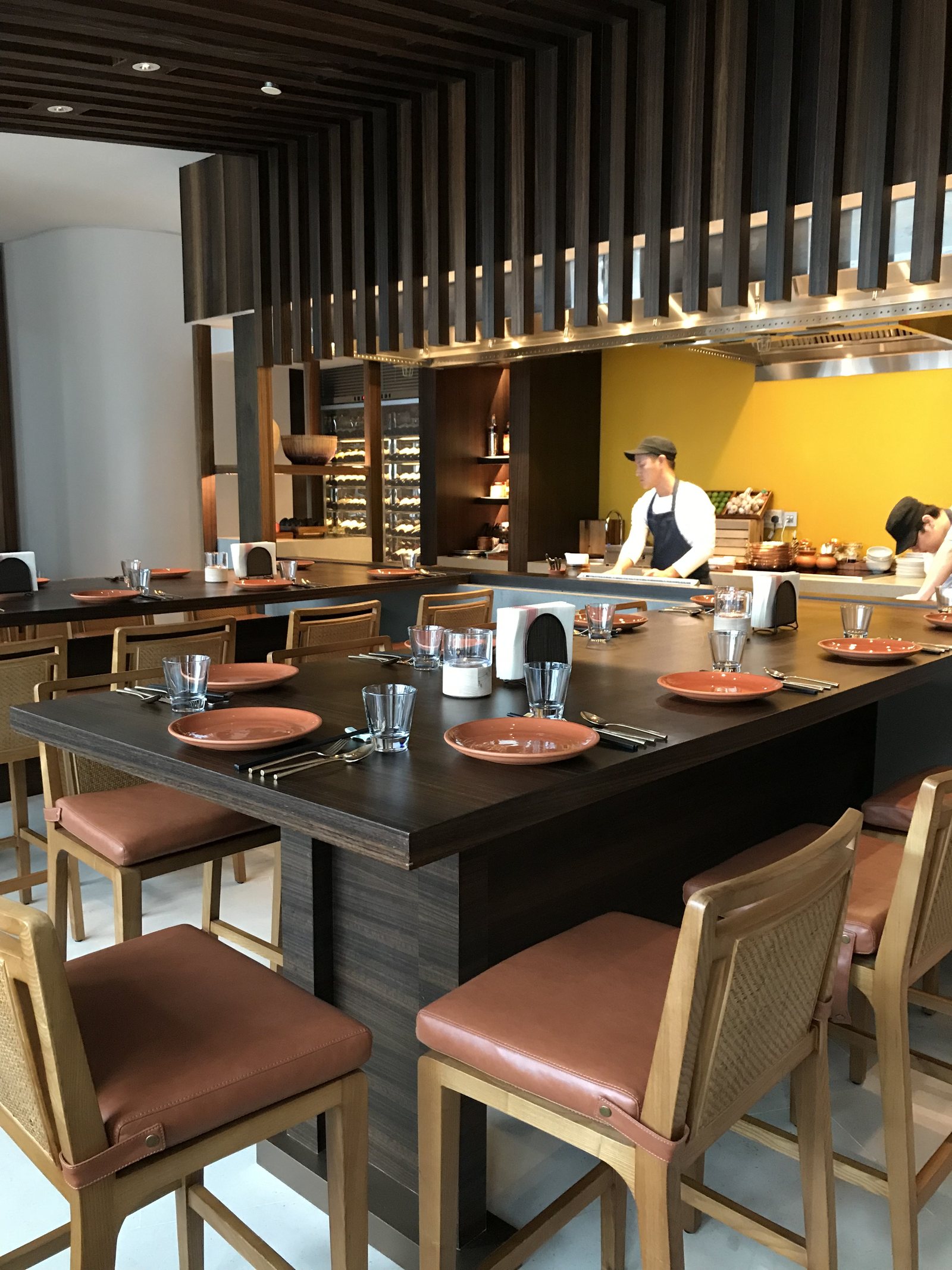 An open kitchen counter with a chef working behind it, stools set along the front