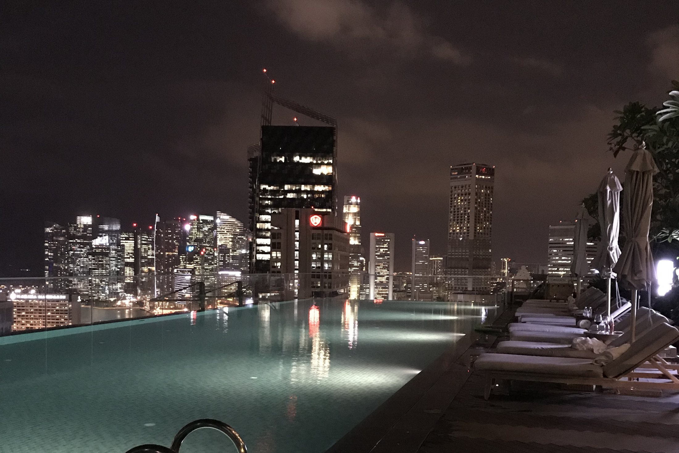The infinity pool lit from within at night, the towers of Singapore standing behind it