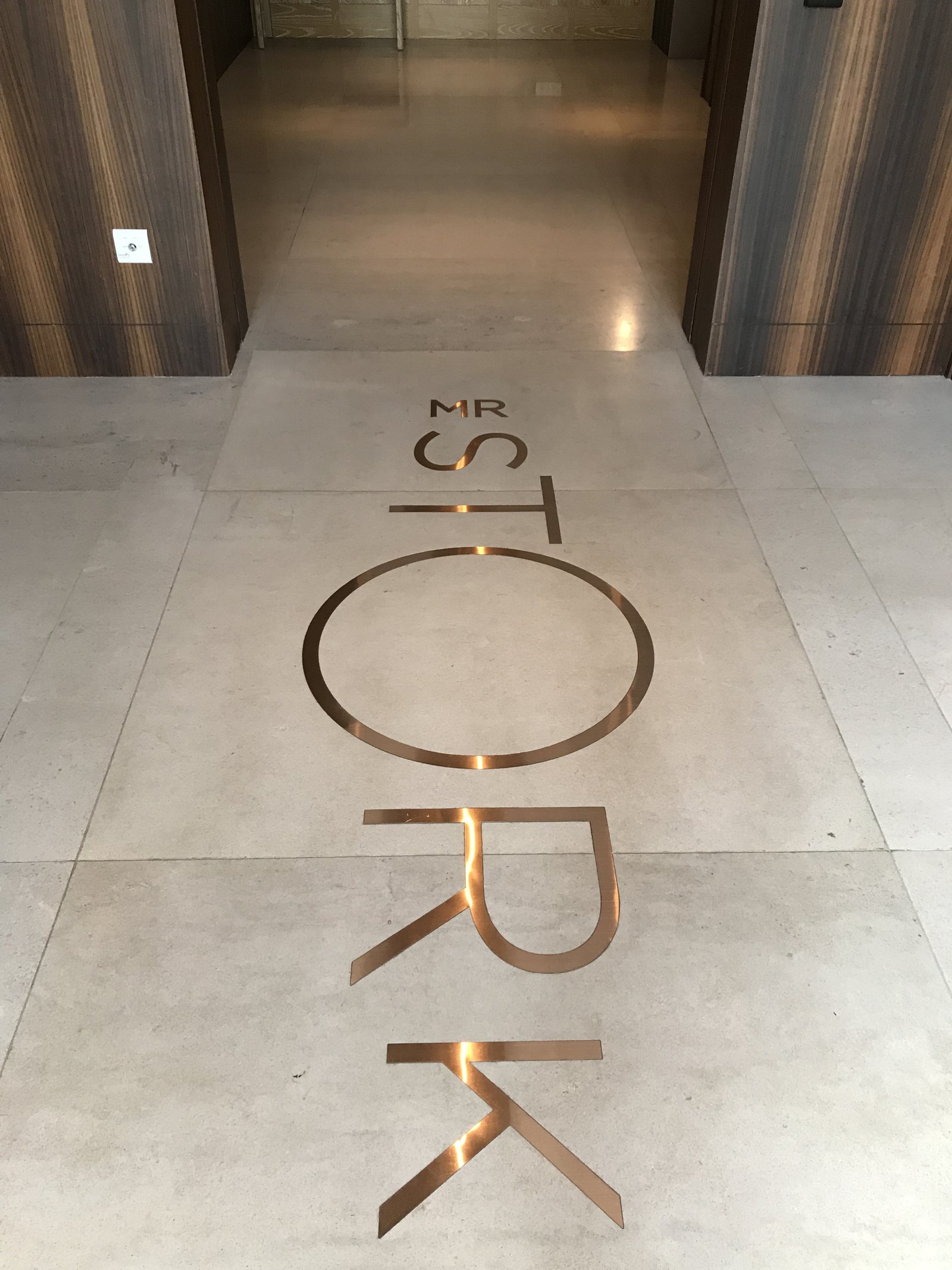 MR STORK inlaid in brass letters across a pale stone floor between lift doors