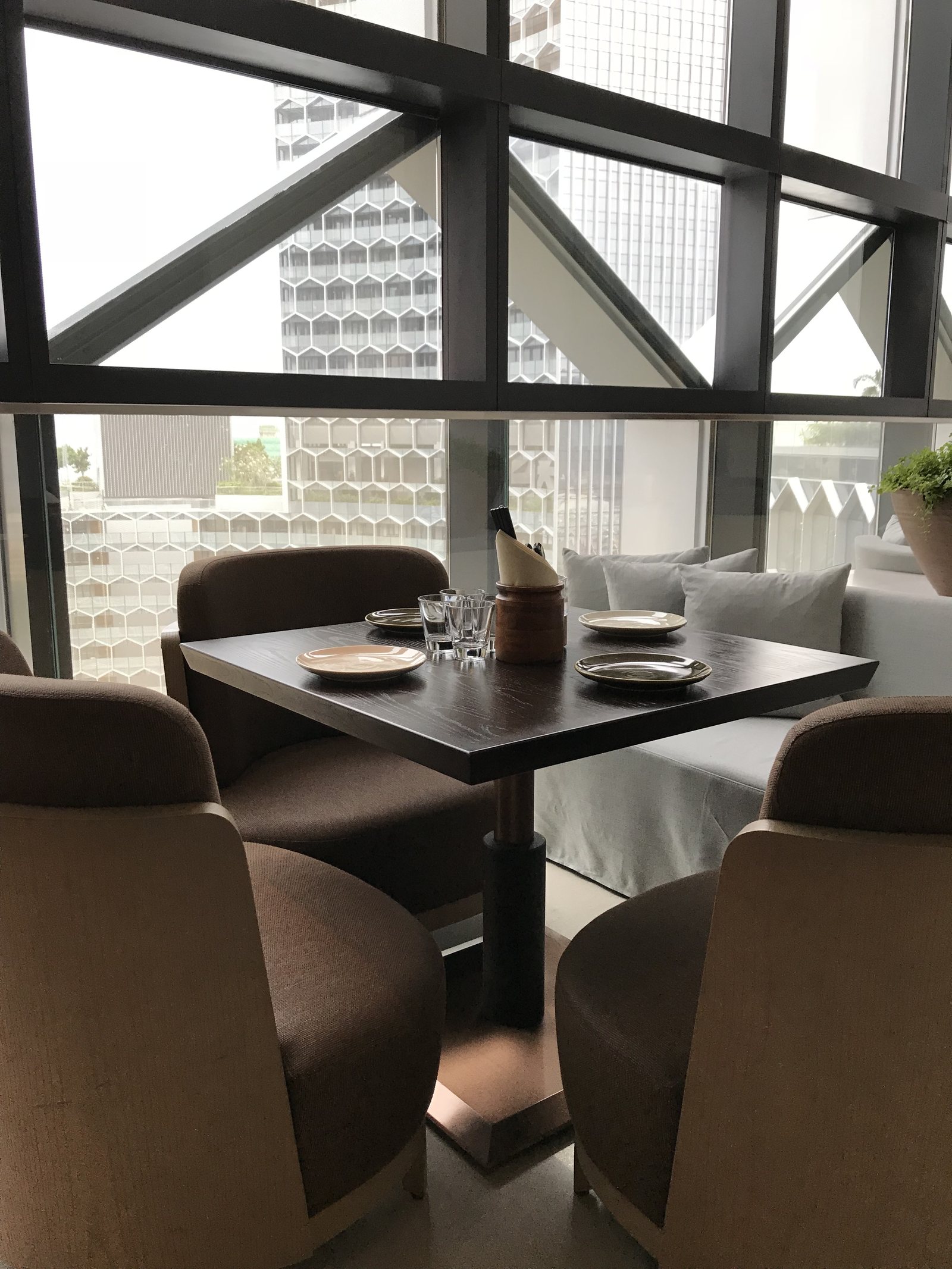 A corner table with brown leather chairs under a glass roof, the city outside