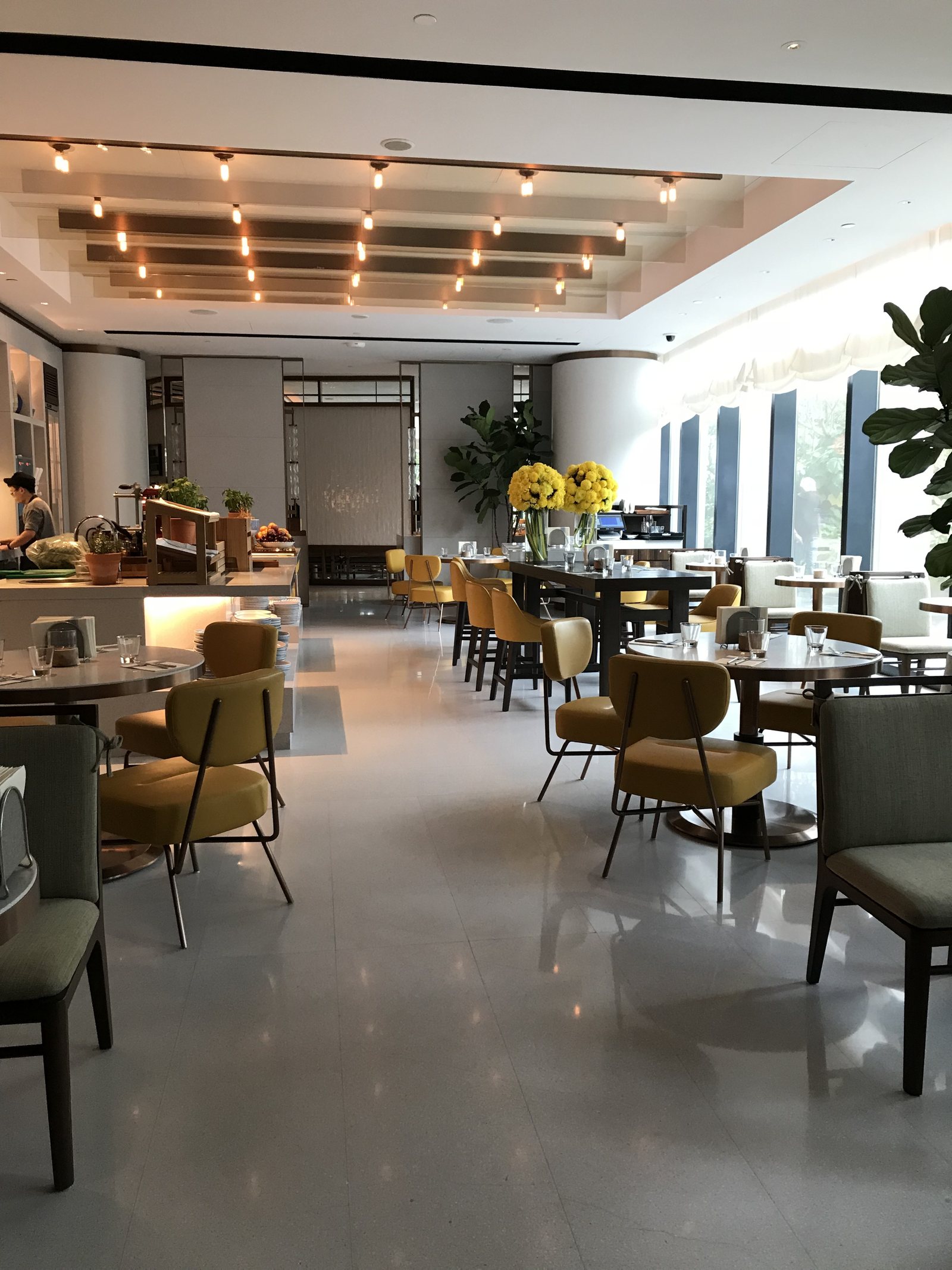 A bright room with mustard and olive chairs, a buffet counter and tall windows