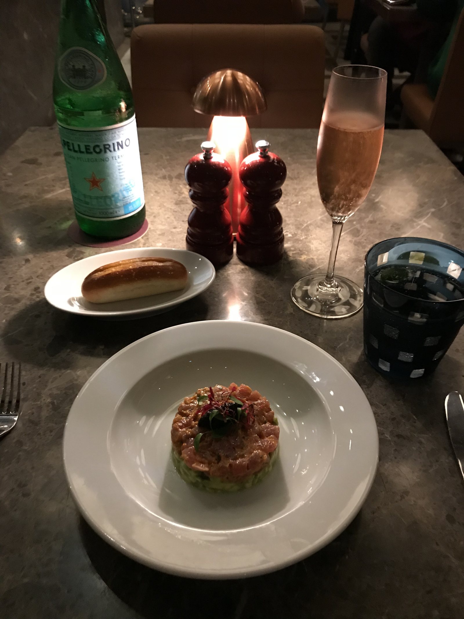 A round of tuna tartare on avocado on a white plate, with bread and a flute beside it