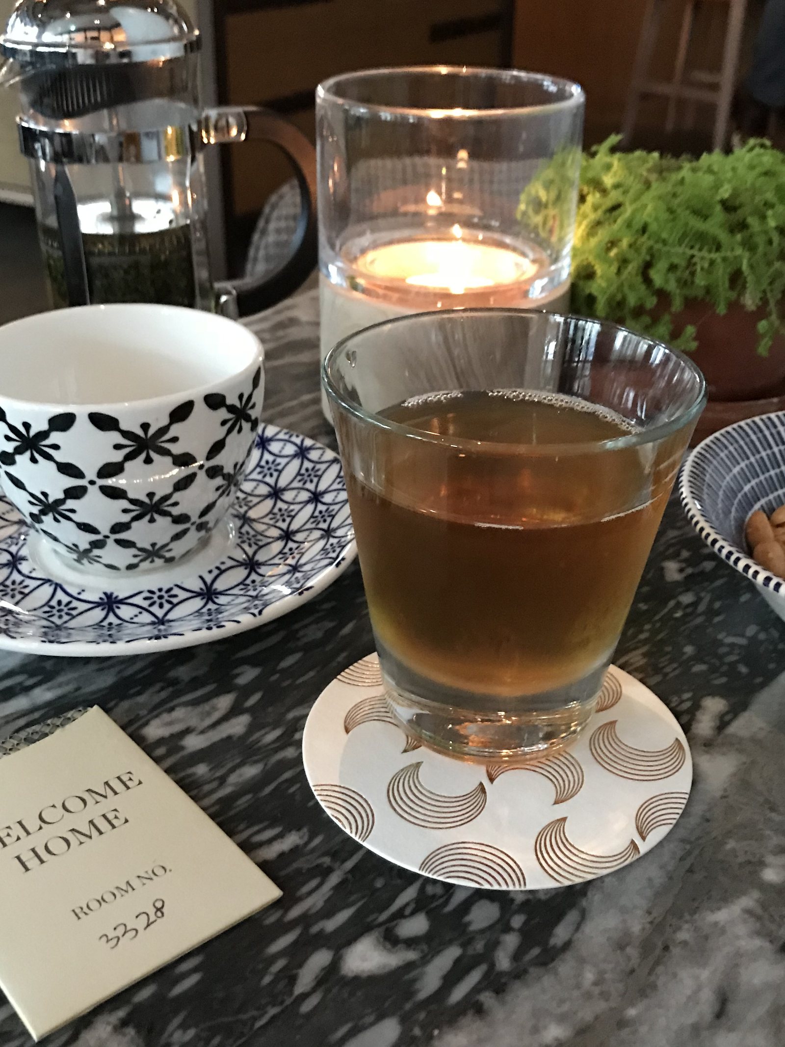 A cup of tea and a glass on a marble table beside a welcome card and a small plant