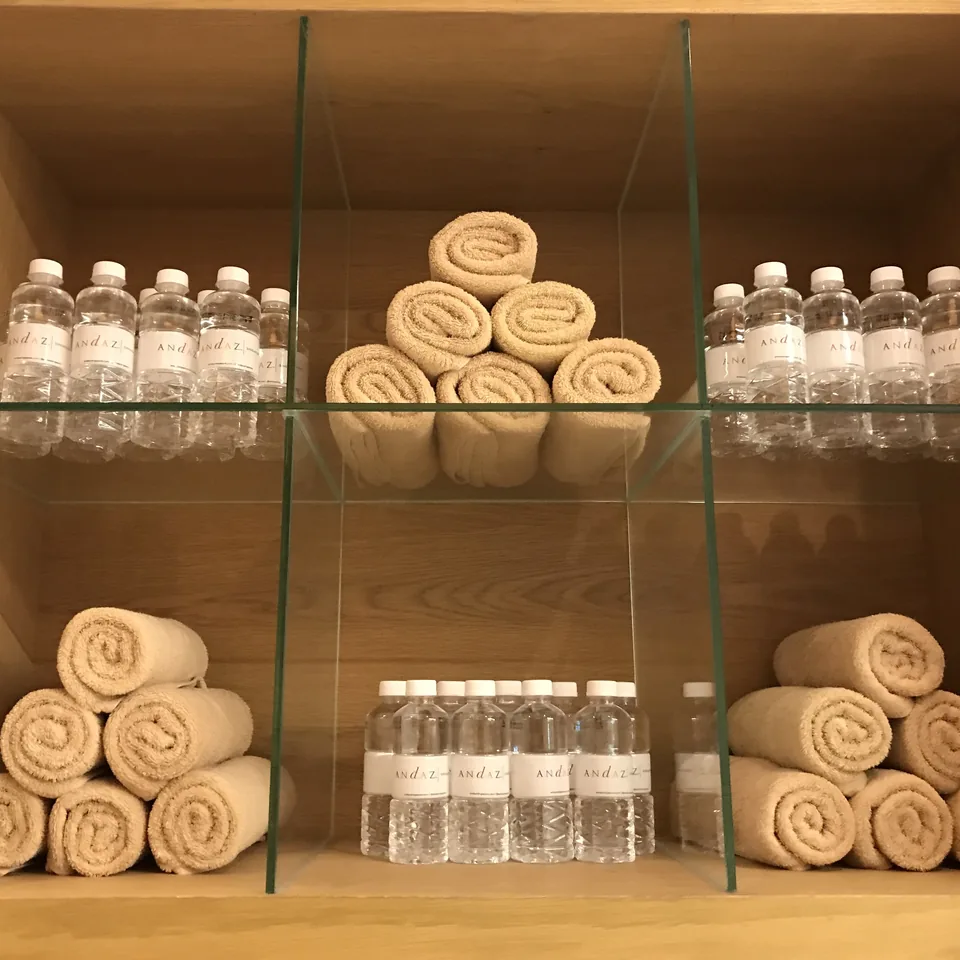 Rolled towels and bottles of water on glass shelves in a timber recess