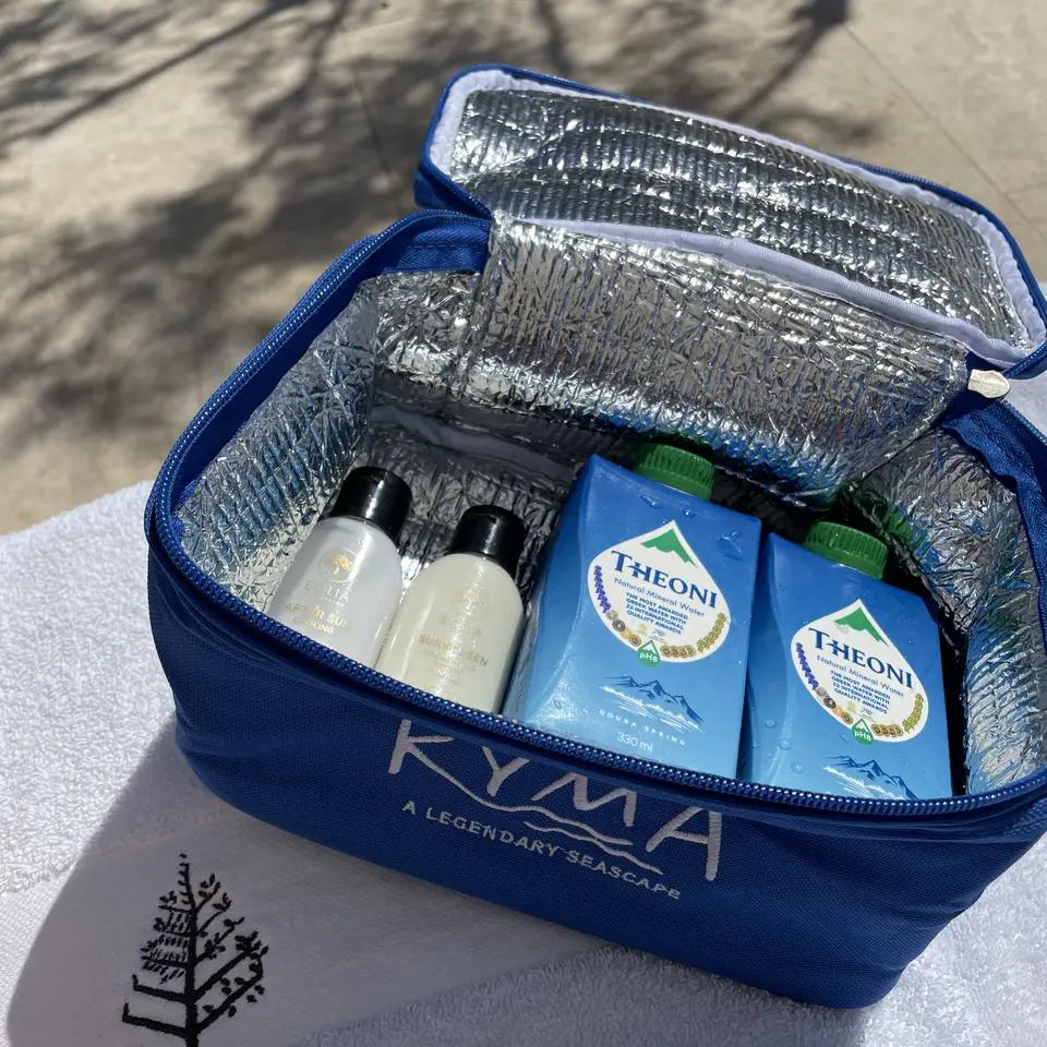 A beach bag with water bottles and sun cream on a folded towel