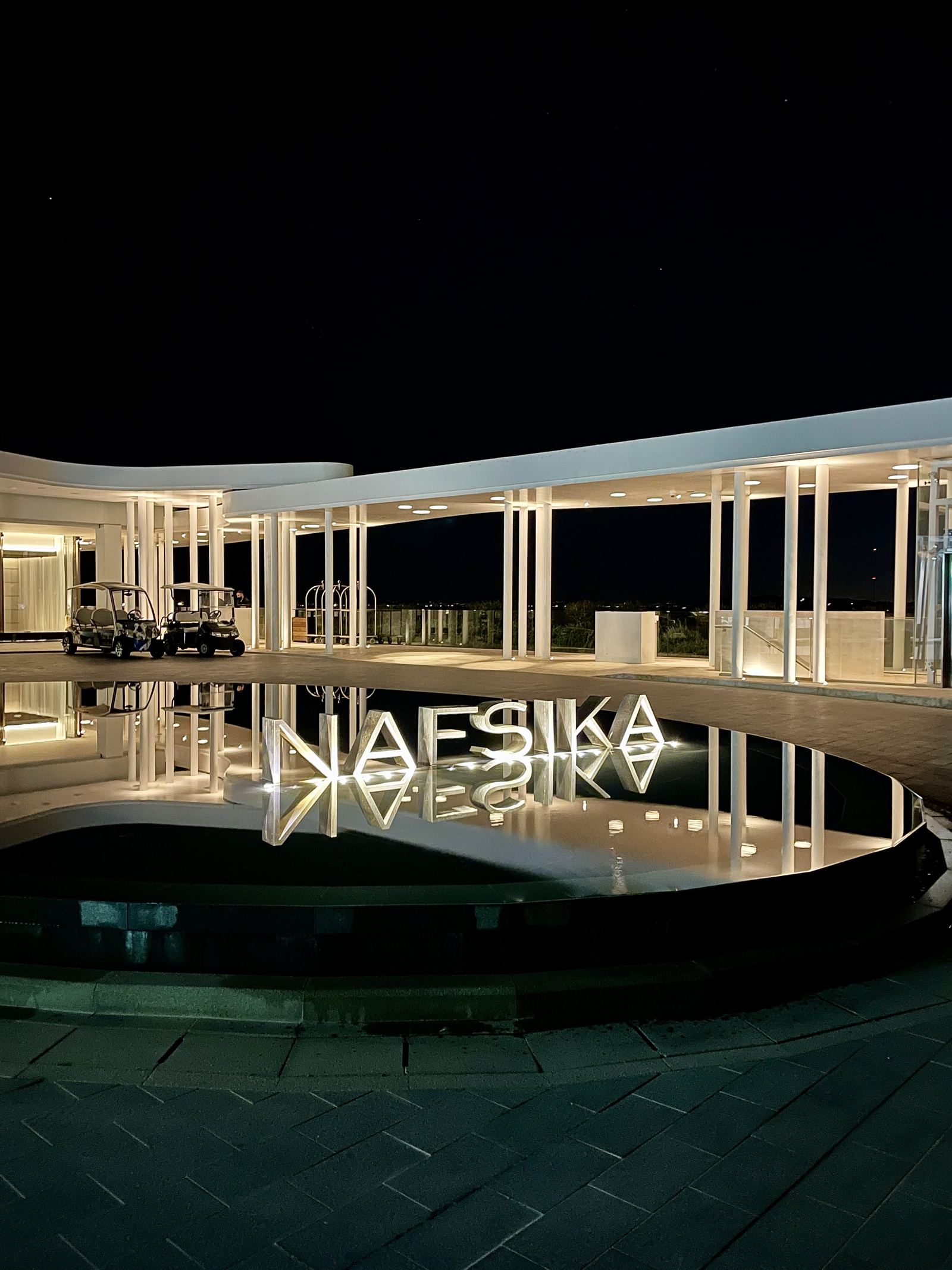 The Nafsika building lit at night and reflected in the entrance pool