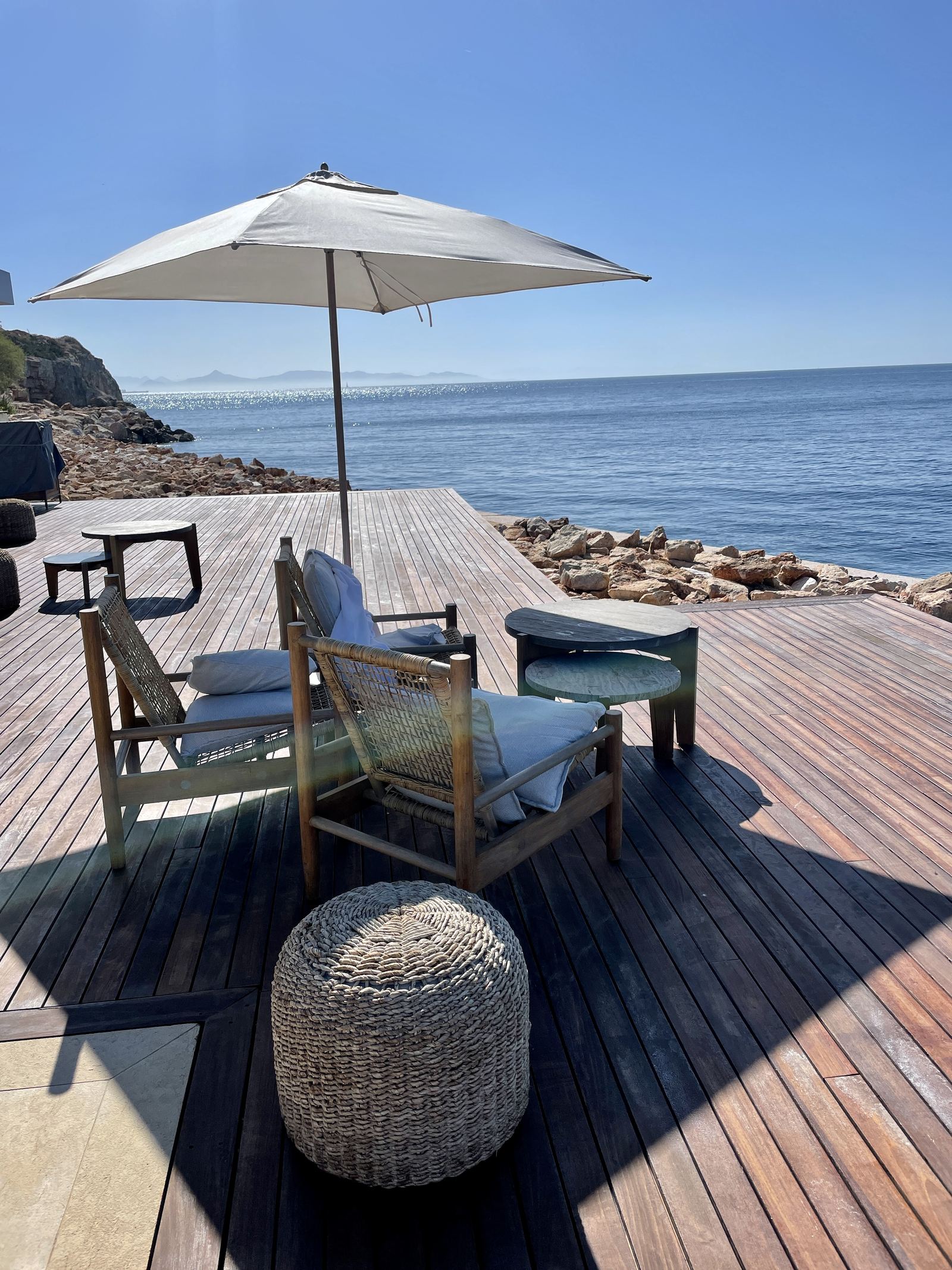 A timber deck with chairs set over the rocks above the water
