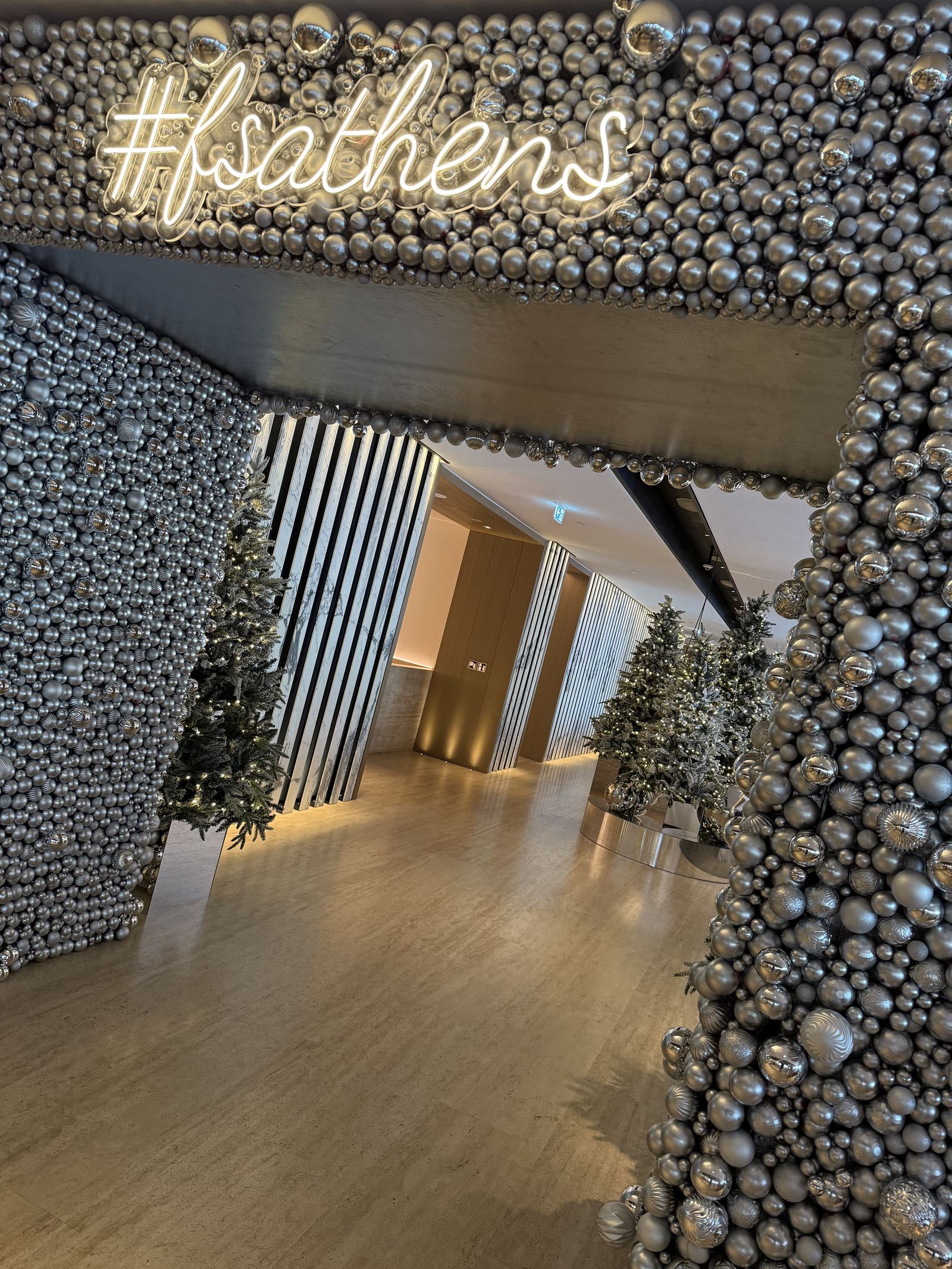 A wall of silver baubles and a neon sign reading hashtag fsathens in the Nafsika lobby