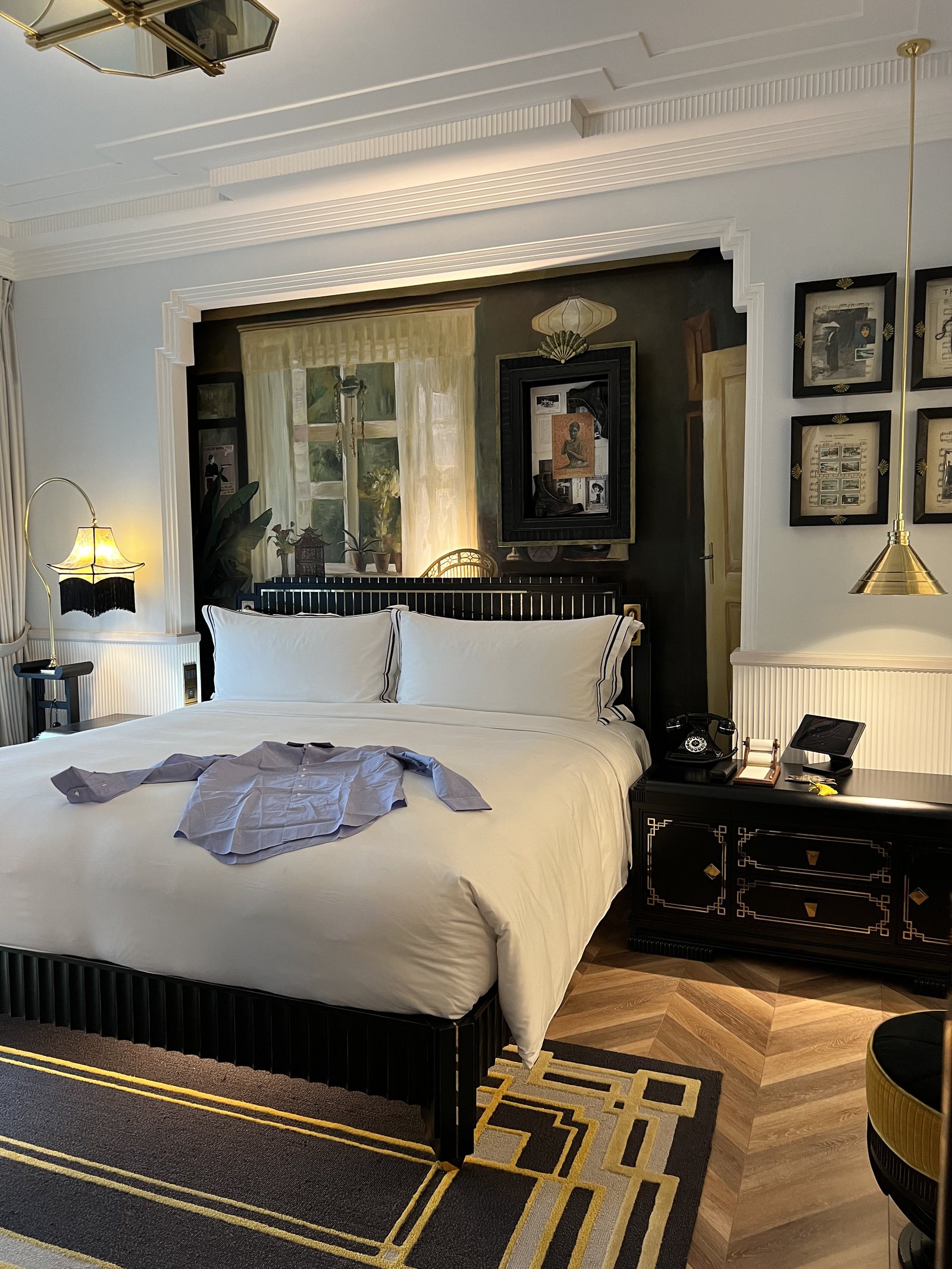A made bed with a folded pair of pyjamas laid across it and framed pictures on the wall behind
