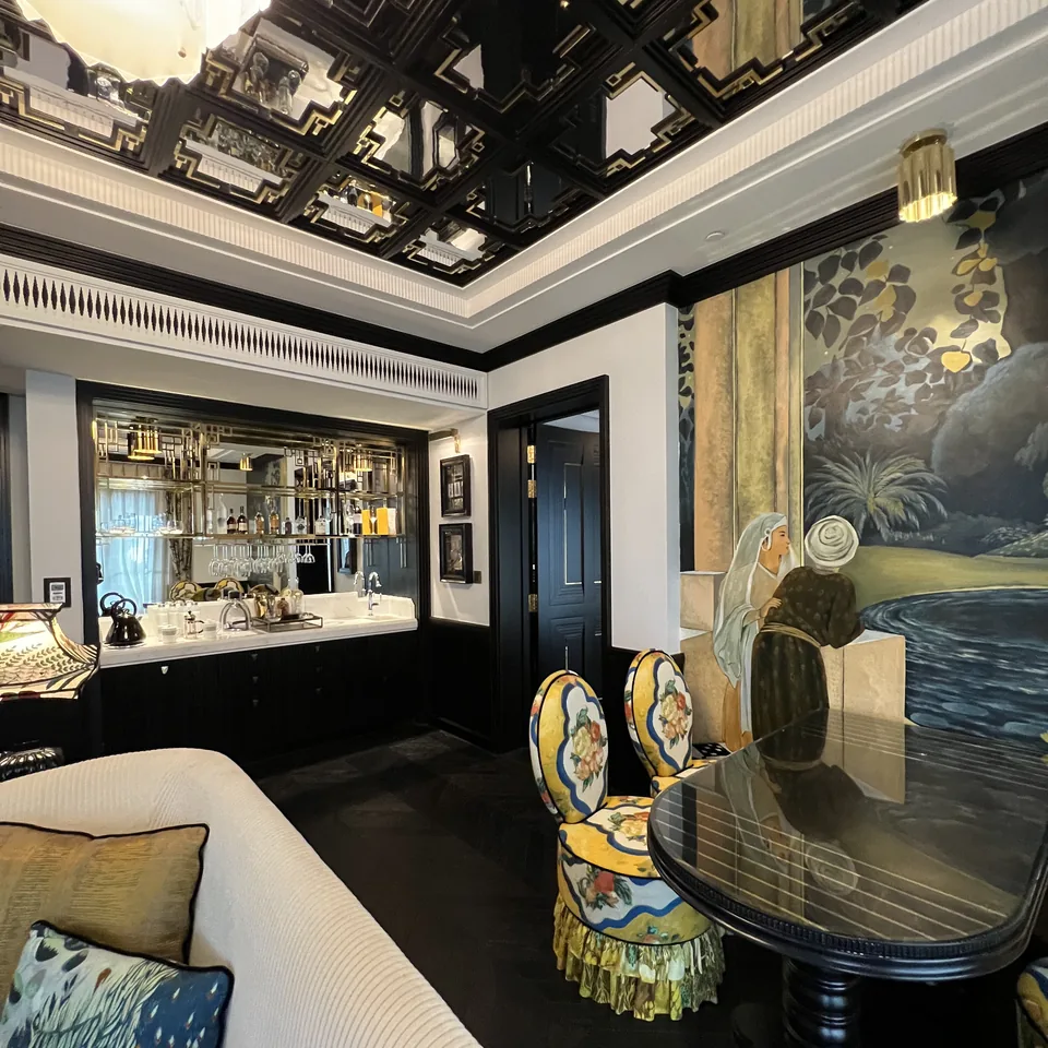 A cream sofa and two patterned chairs in a suite salon, beside a bar and a painted screen