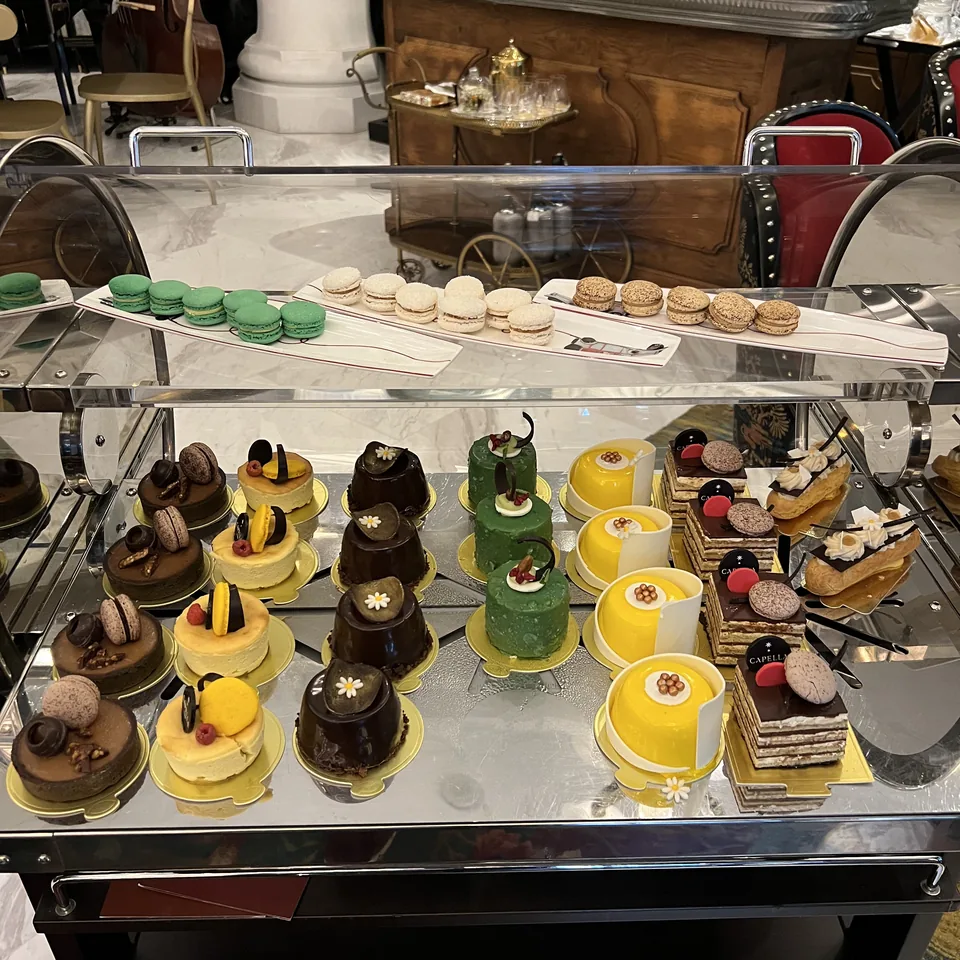 A mirrored trolley of pastries and macarons in rows, under a bar lined with bottles
