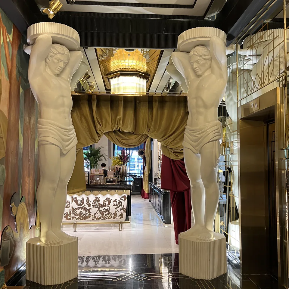 Two carved white figures standing either side of an opening, with a gold curtain and a sofa beyond