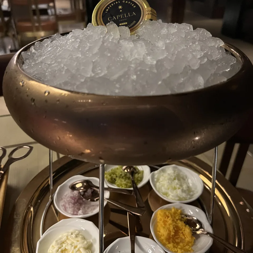 A brass stand holding a bowl of crushed ice above small dishes of chopped egg, onion and herbs