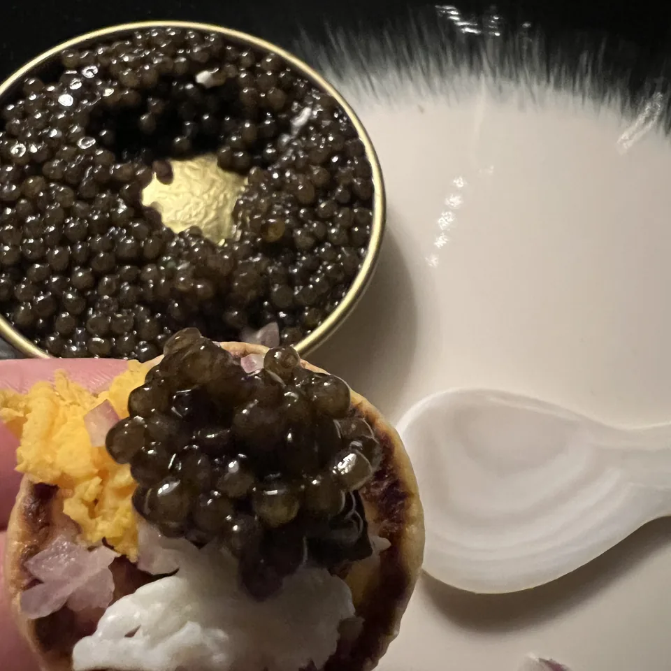 A tartlet topped with caviar beside an open tin, on a black lacquer surface