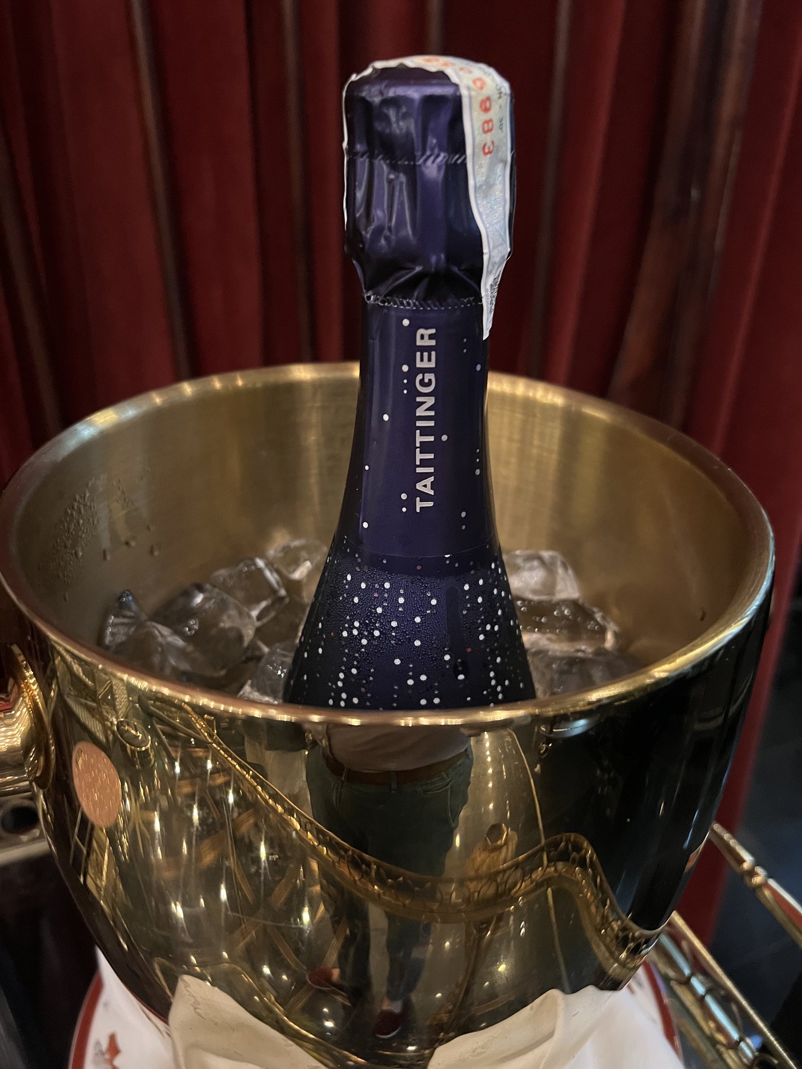 A bottle of Taittinger in a brass ice bucket in front of a red velvet curtain