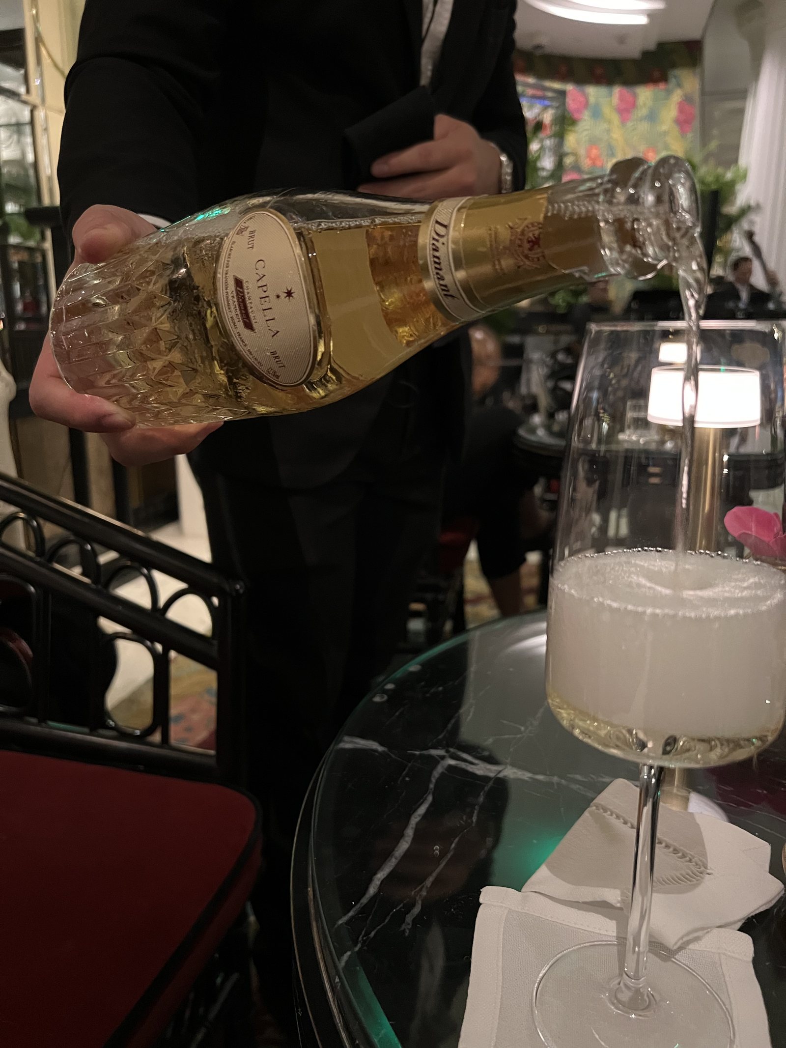 A glass being filled with champagne at a dark marble table, poured by a waiter in black