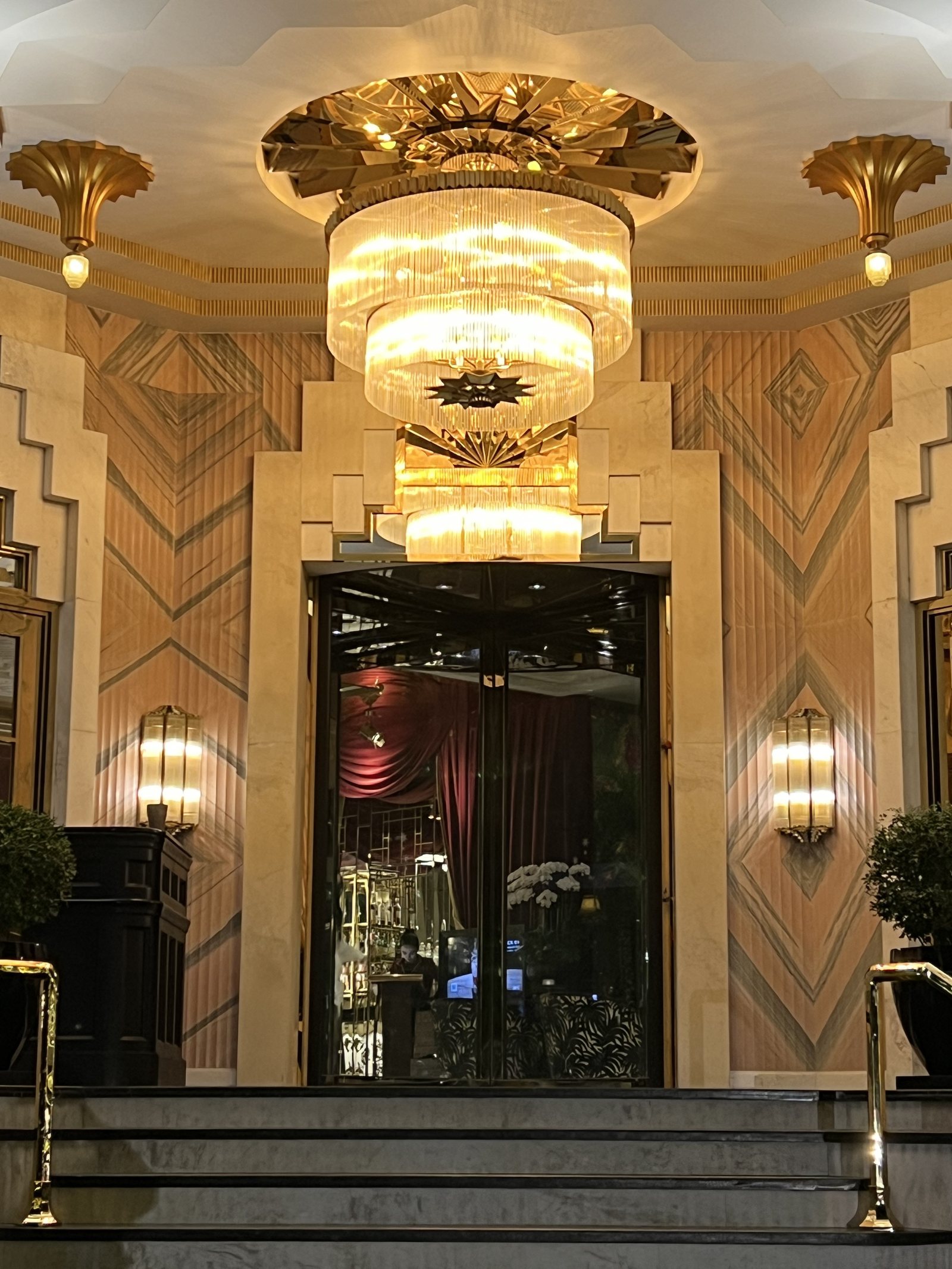 A tiered glass chandelier under a gilded ceiling rose, above a mirrored doorway