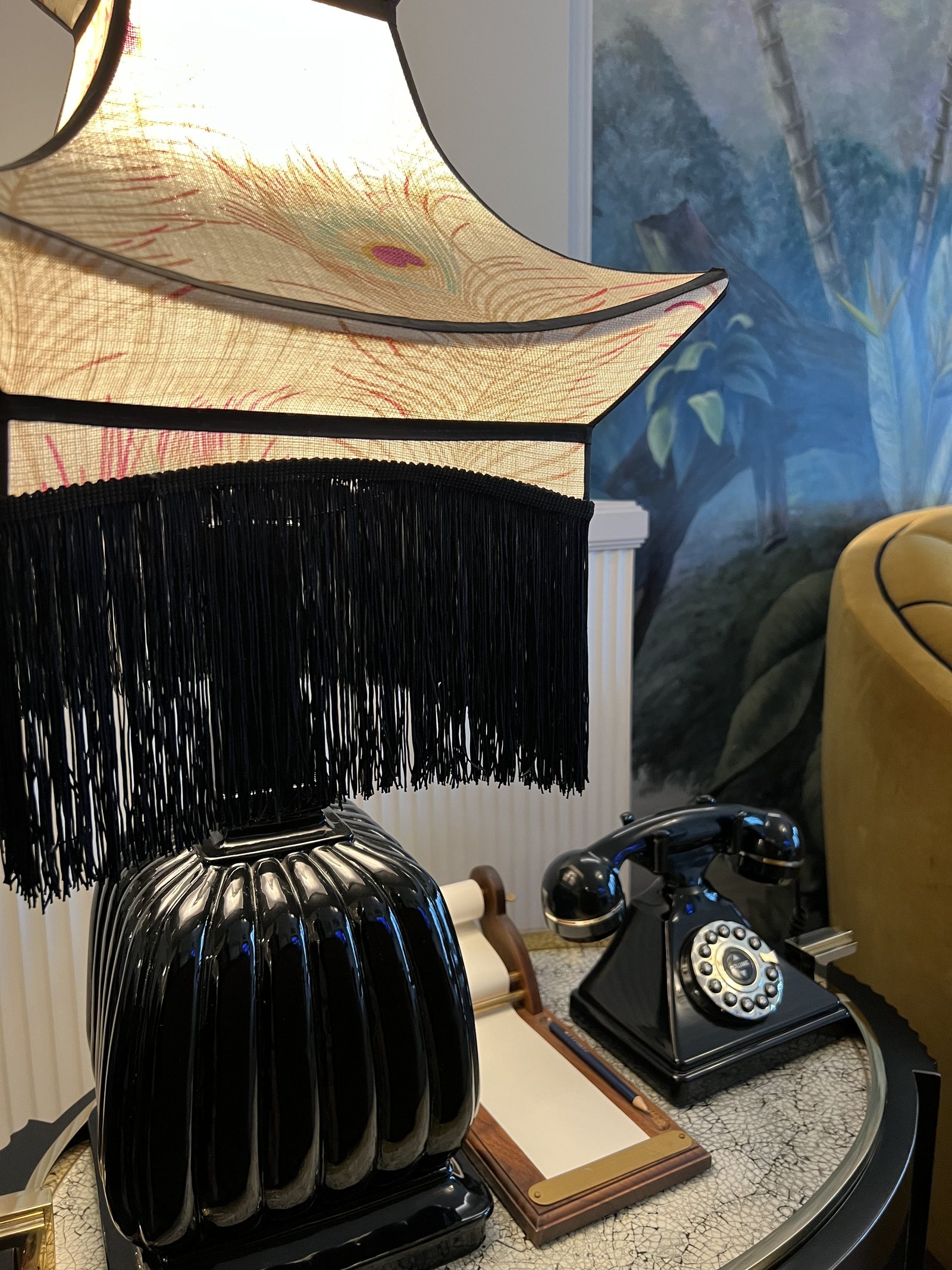 A black fringed lamp beside a black rotary telephone on a side table, against a painted wall
