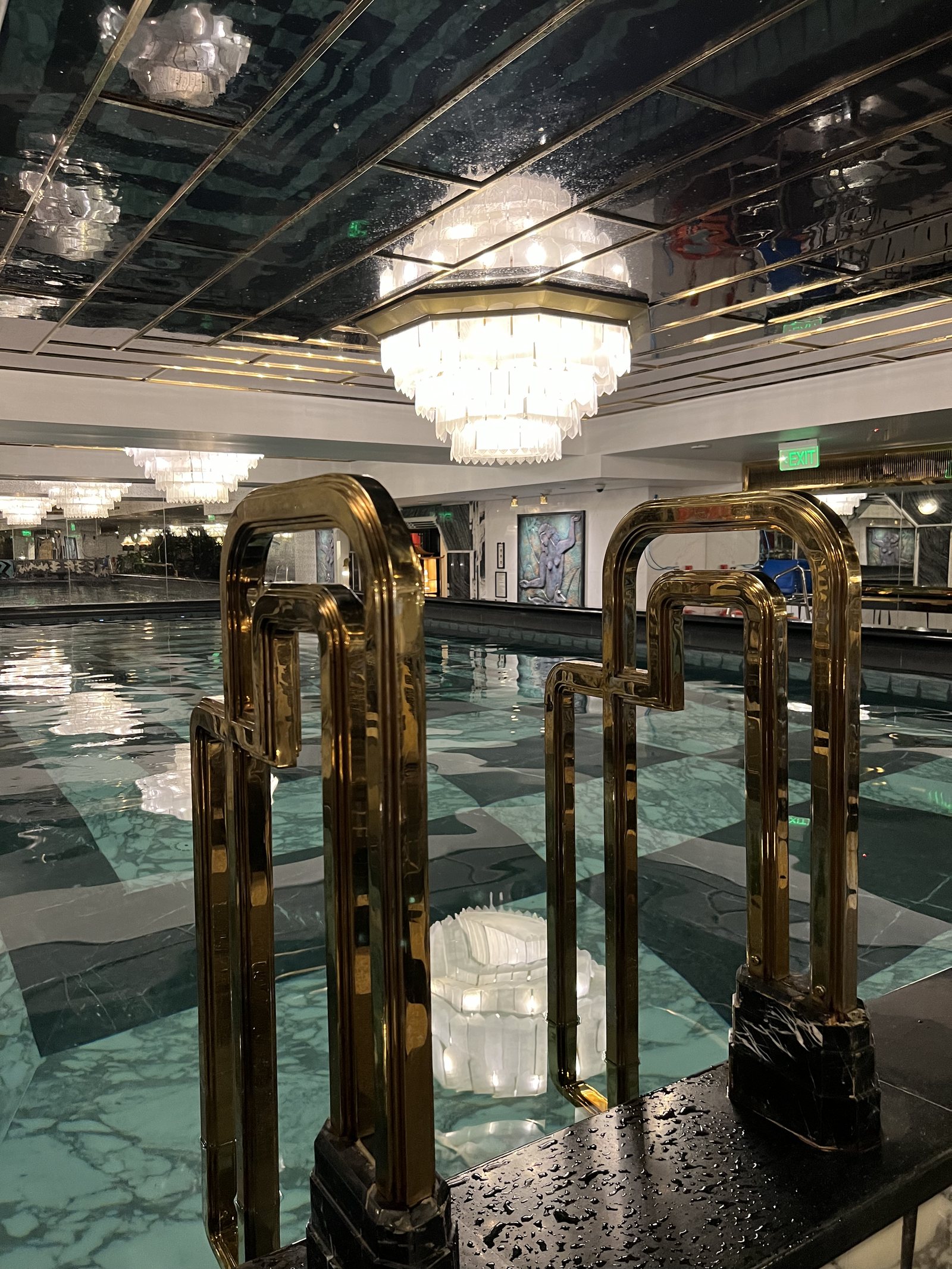 The brass ladder rails at the edge of the long indoor pool, with a tiered glass chandelier above and a mirrored ceiling