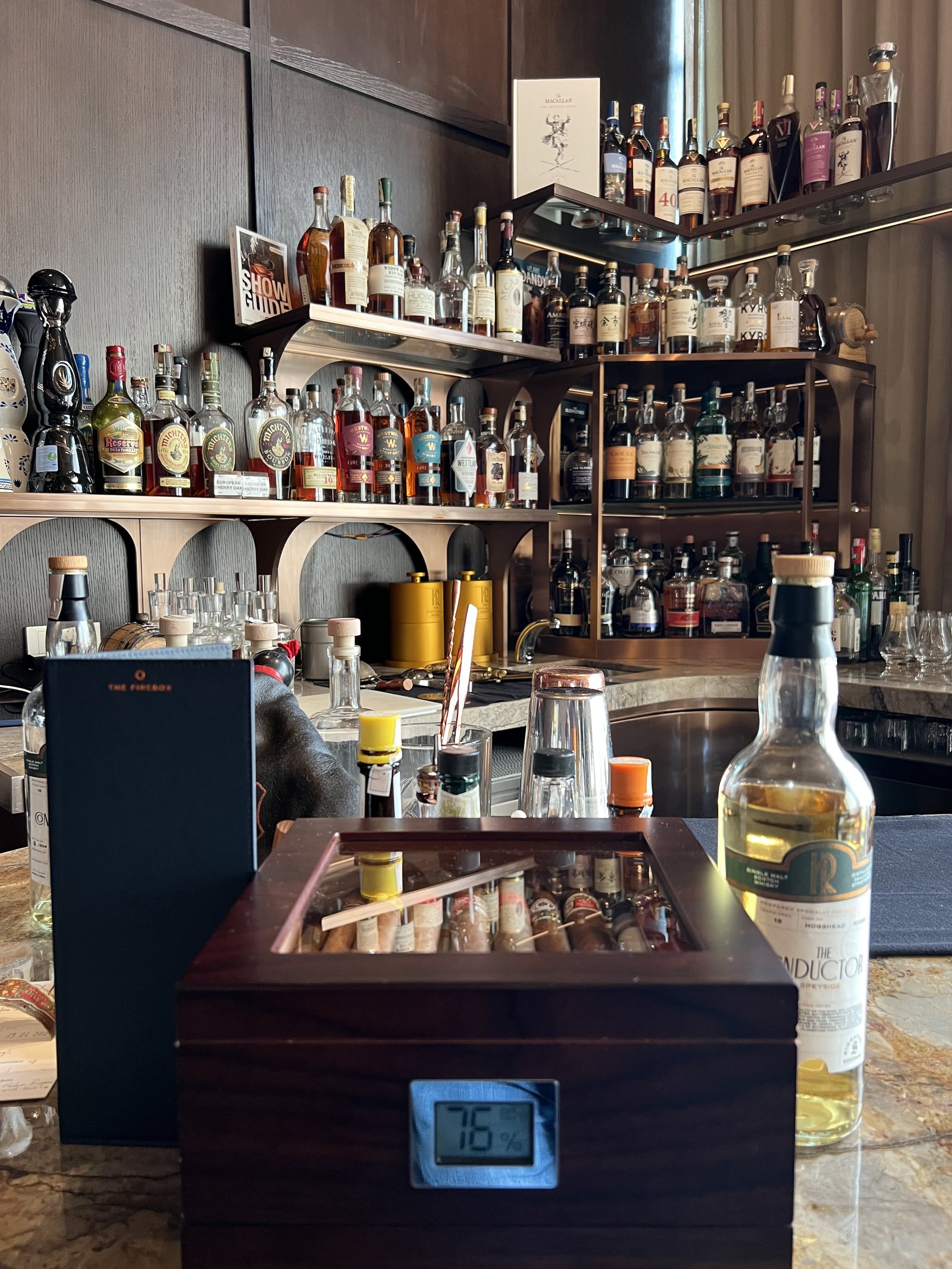 Shelves of spirits above a wooden humidor cabinet with a hygrometer on its front