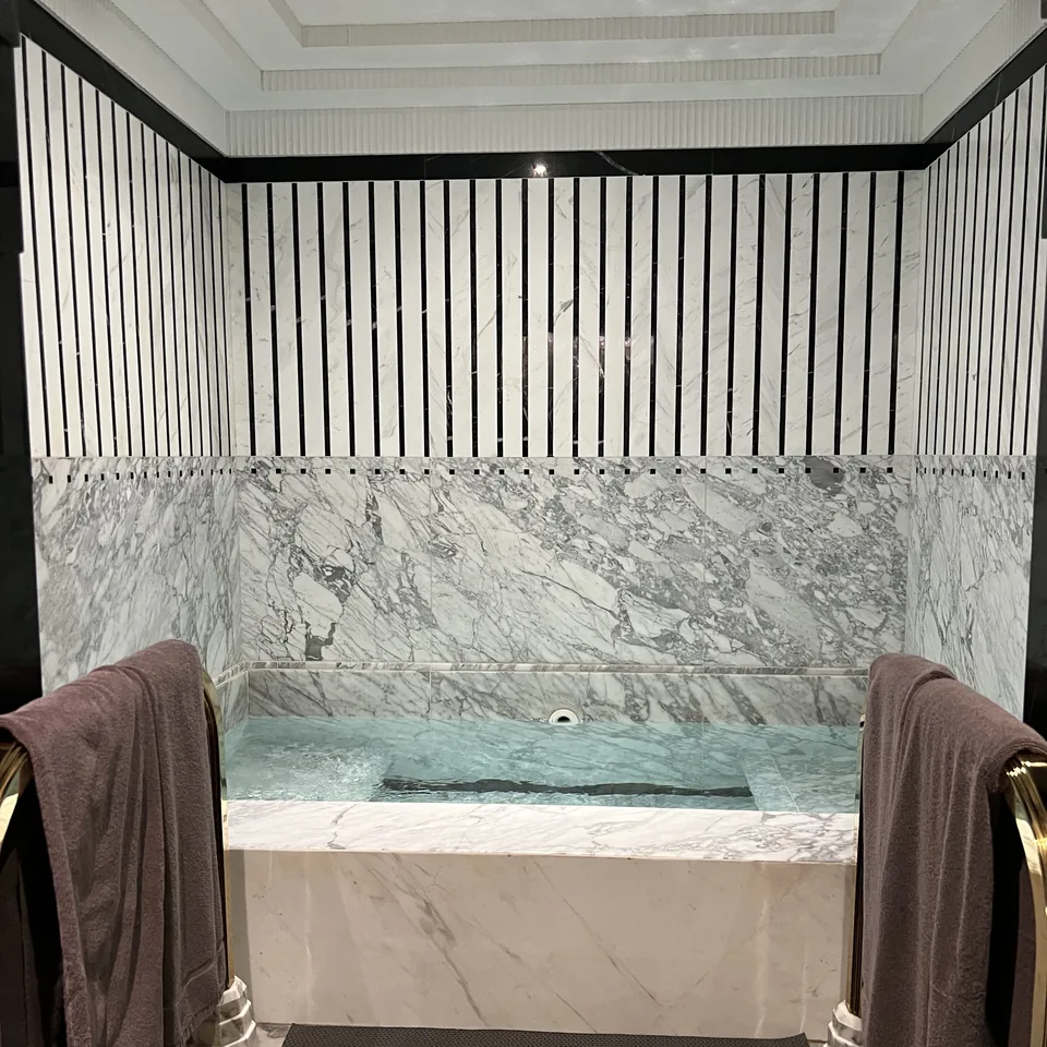 A marble hydrotherapy bath set into a panelled wall, with towels folded over the rails on either side