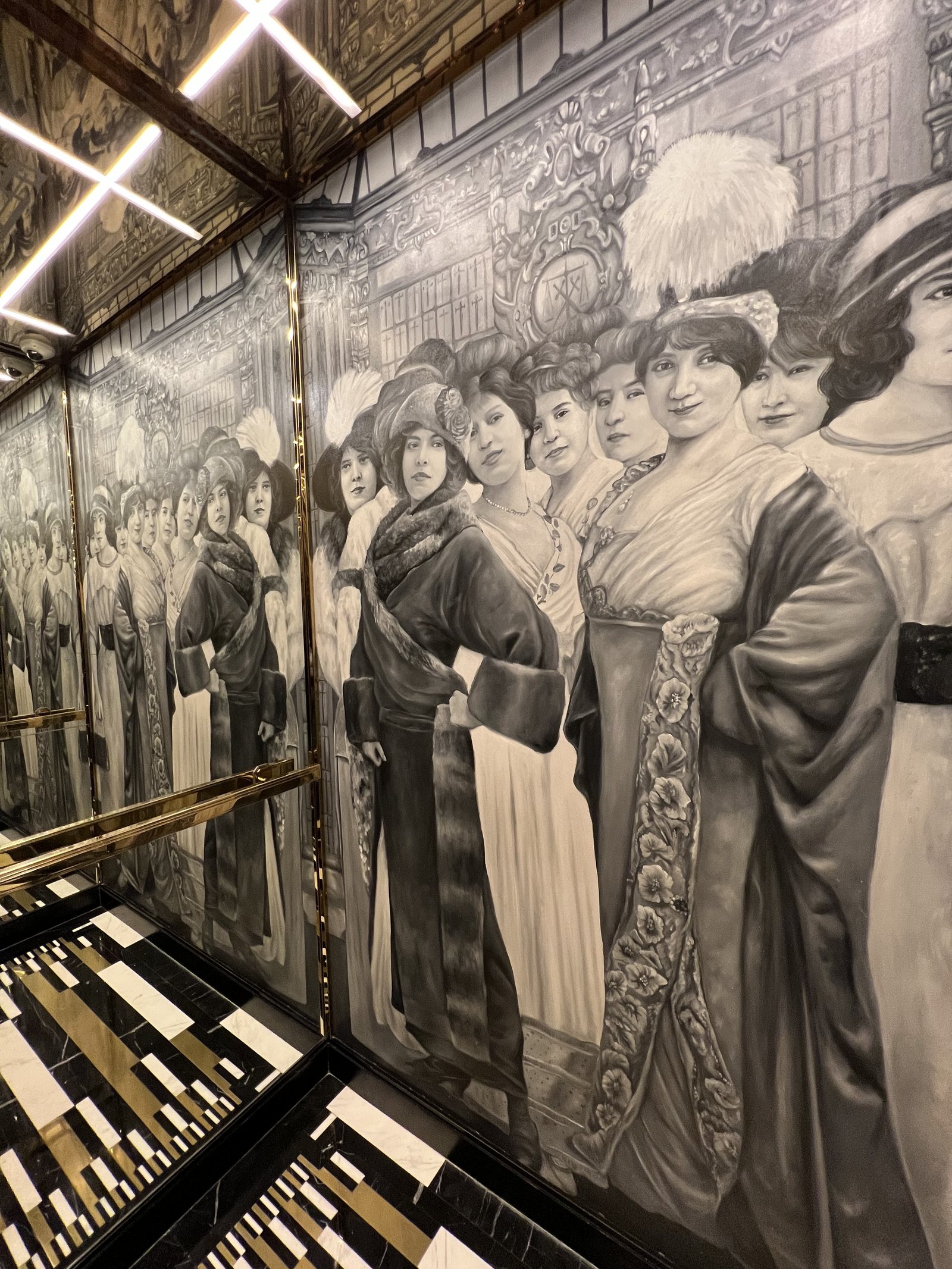 A full-height grey mural of women in wide hats and fur collars, above a striped marble floor