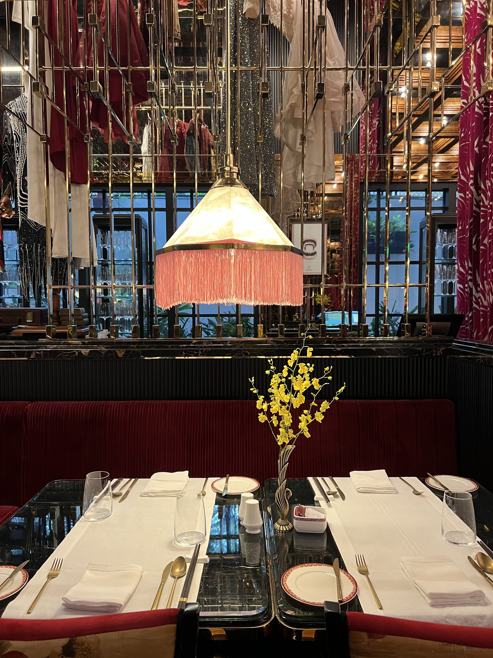 A table laid with white linen, a fringed pendant lamp above it and a spray of yellow blossom in a vase
