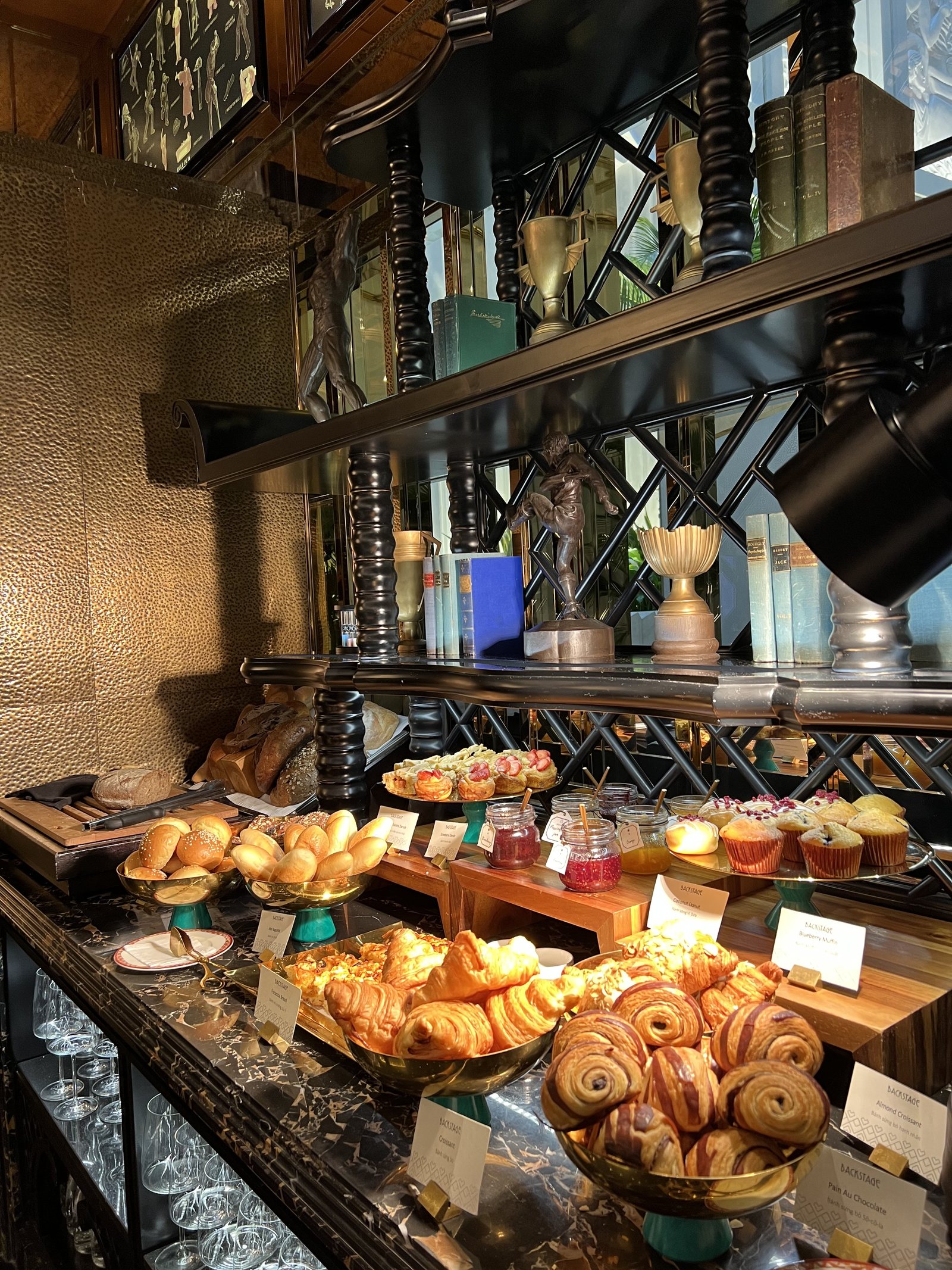 A counter of croissants, pains au chocolat and small cakes under brass shelving