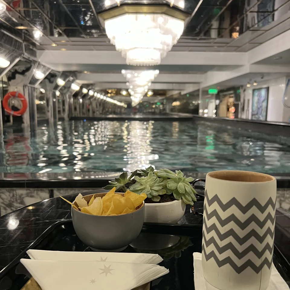 A tray at the poolside with a bowl of crisps, a small plant and a chevron-patterned beaker on a napkin