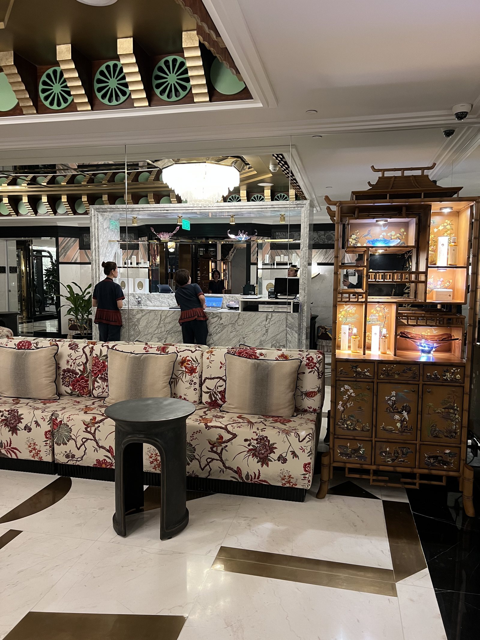 A reception counter in pale marble with a lacquer cabinet beside it and a patterned sofa in front