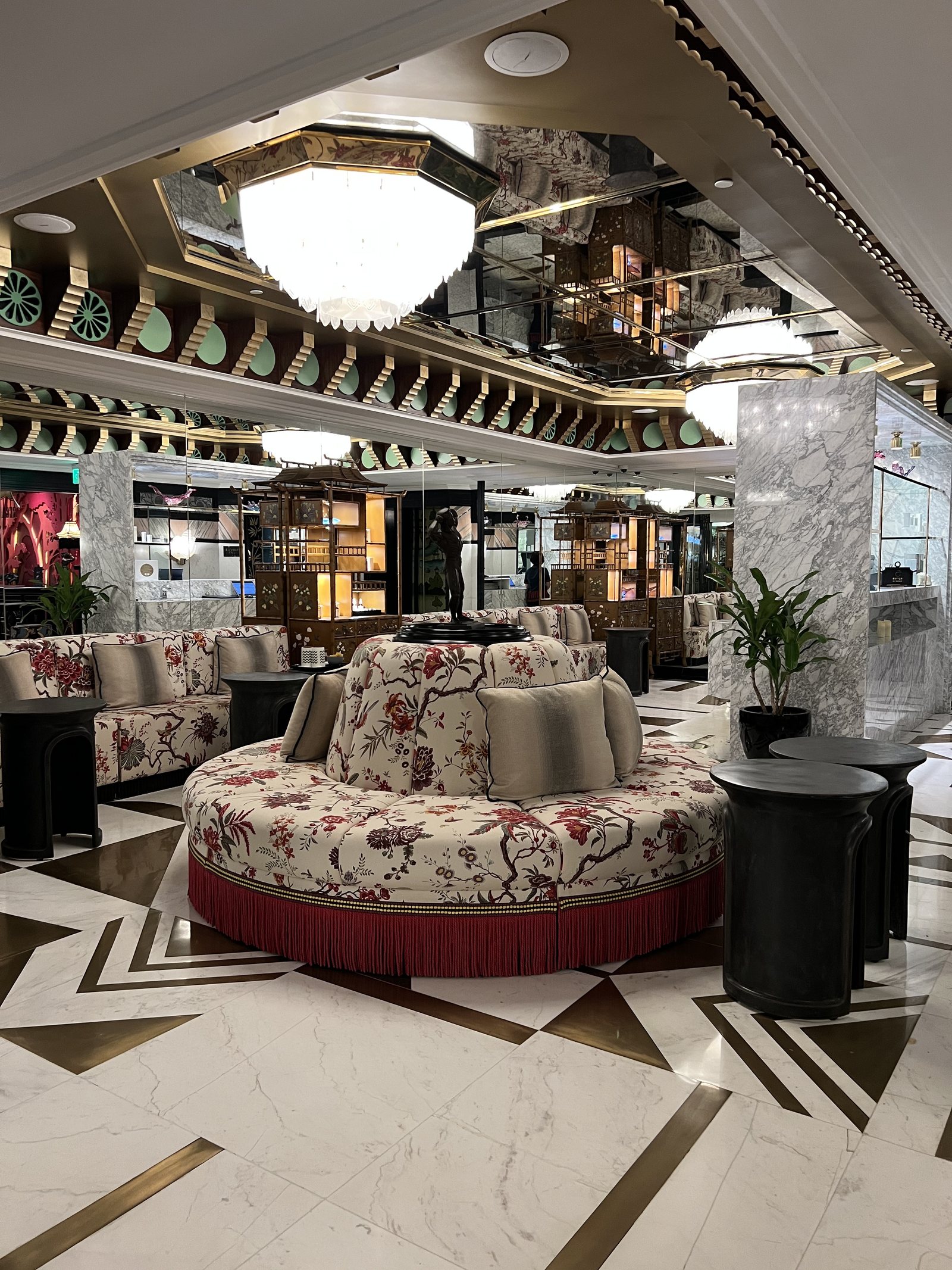 A round floral sofa with a red fringed base at the centre of a marble floor laid in a geometric pattern