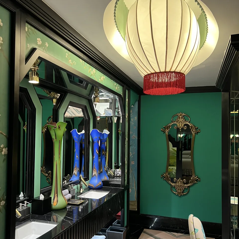 Two basins under mirrors in a green spa washroom, with coloured glass vases on the counter