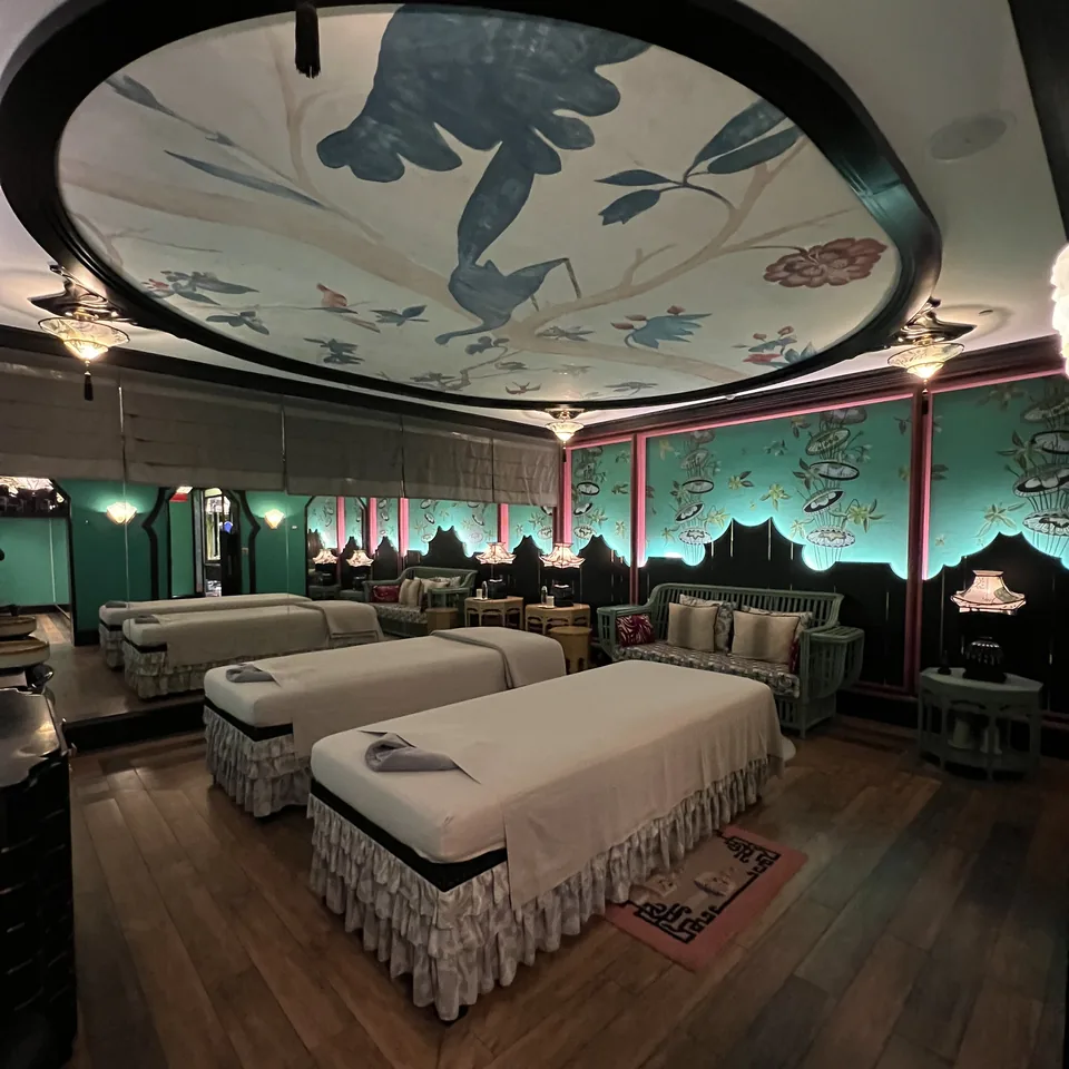 A treatment room with two massage beds side by side, green panelled walls and a painted oval ceiling