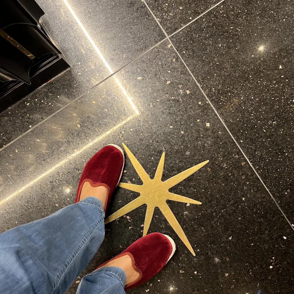 Red velvet slippers standing on a dark terrazzo floor beside a brass star inlaid into the stone