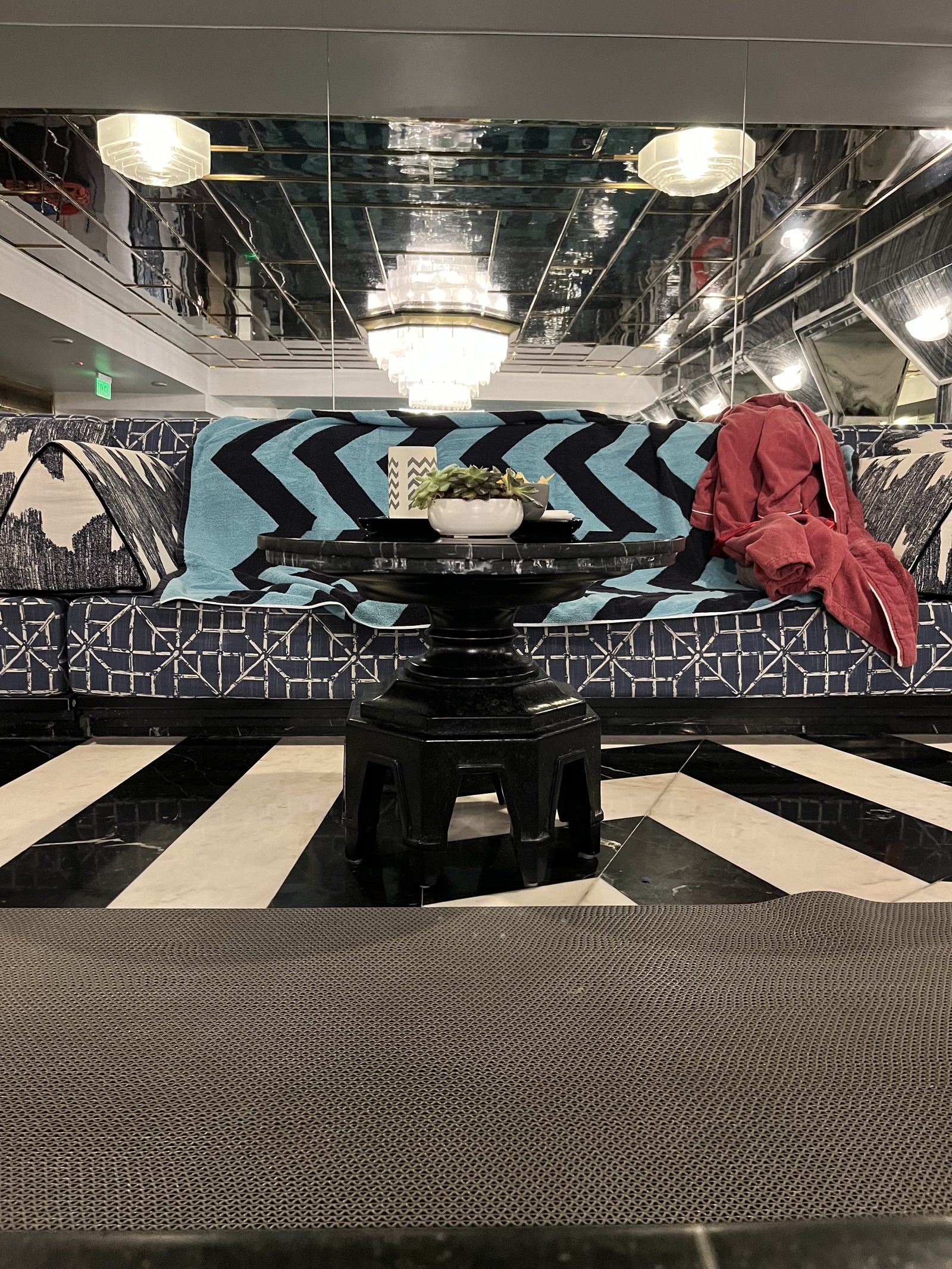 A banquette in blue patterned fabric behind a small round table, on a floor of broad black and white stripes