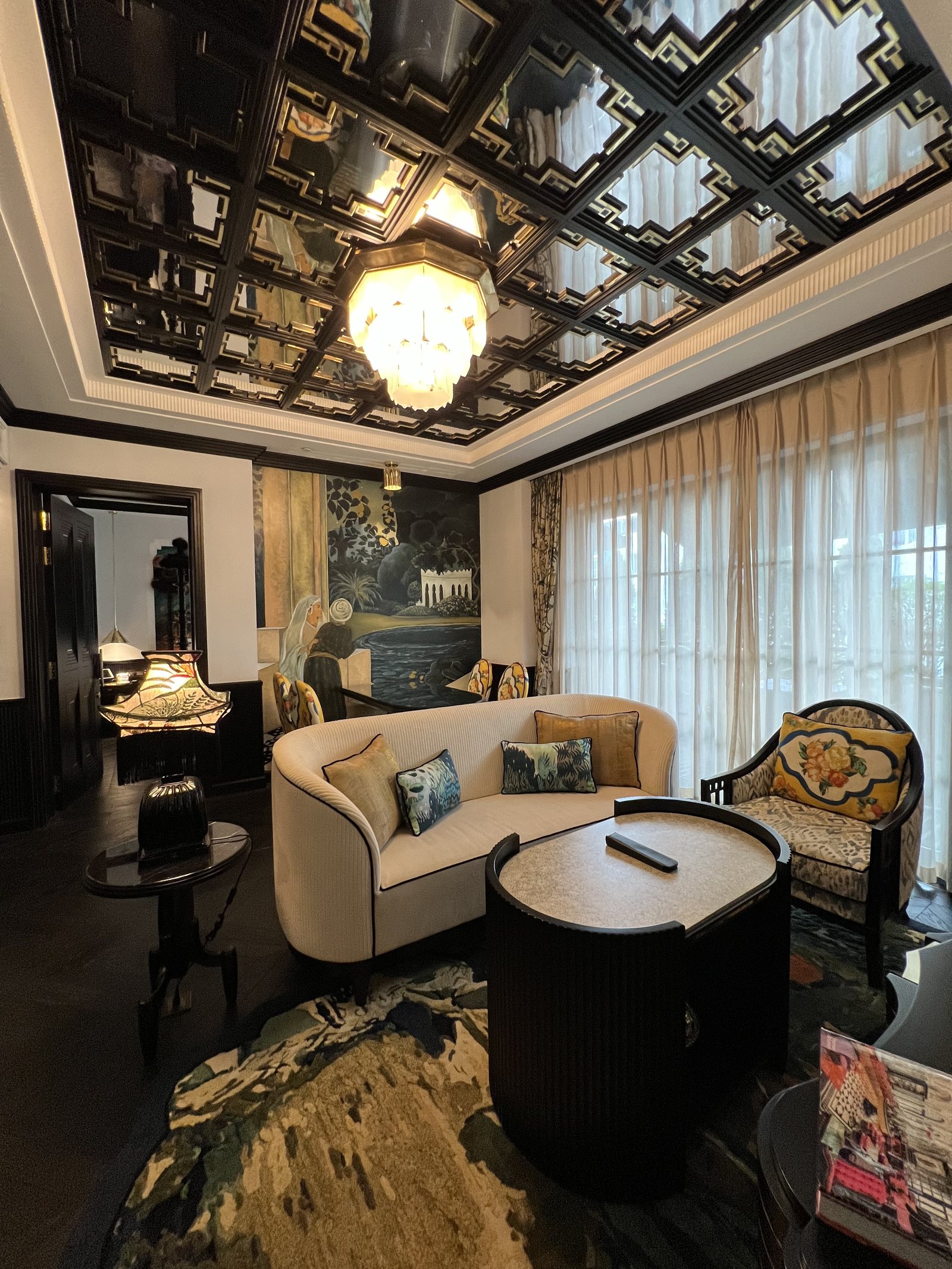 A curved cream sofa and two patterned armchairs around a dark round table, under a mirrored ceiling